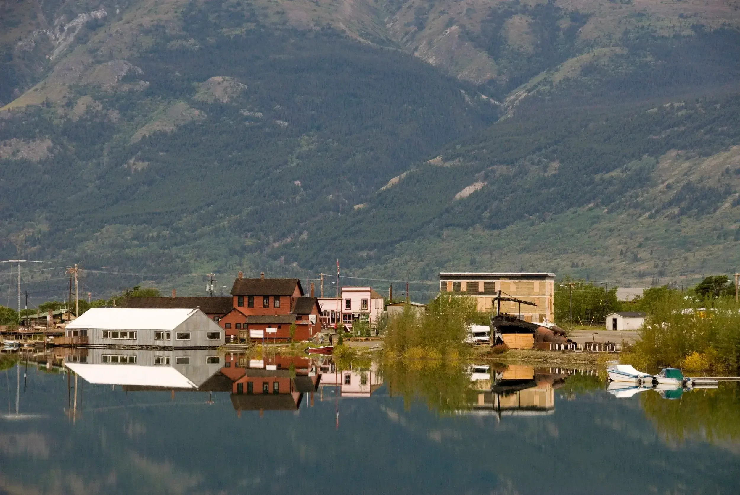 A small lakeside town with colorful houses reflected in the calm water, mountains in the background, and a clear sky.