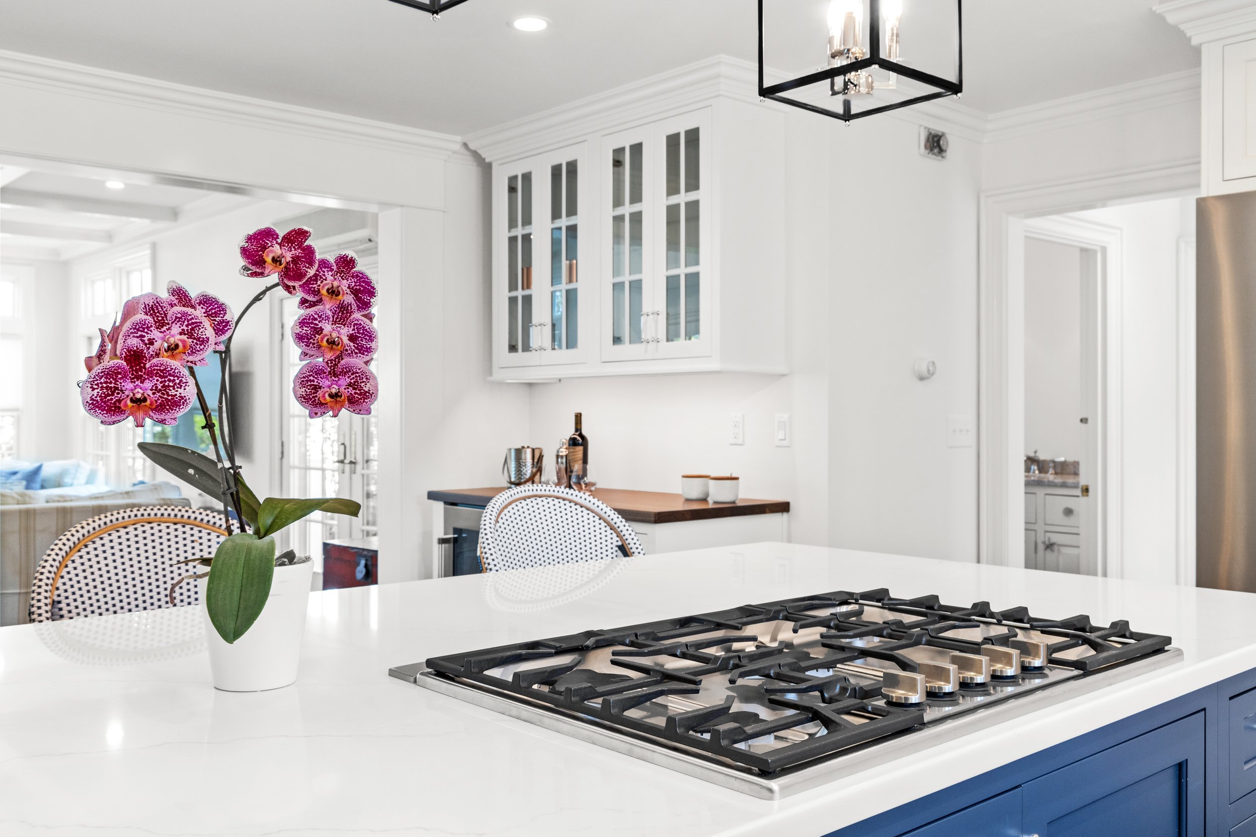 Modern kitchen with white cabinets, gold handles, and a gray countertop. Contains a gas stove with a white marble backsplash, wooden cutting boards, and a window with a view of trees.