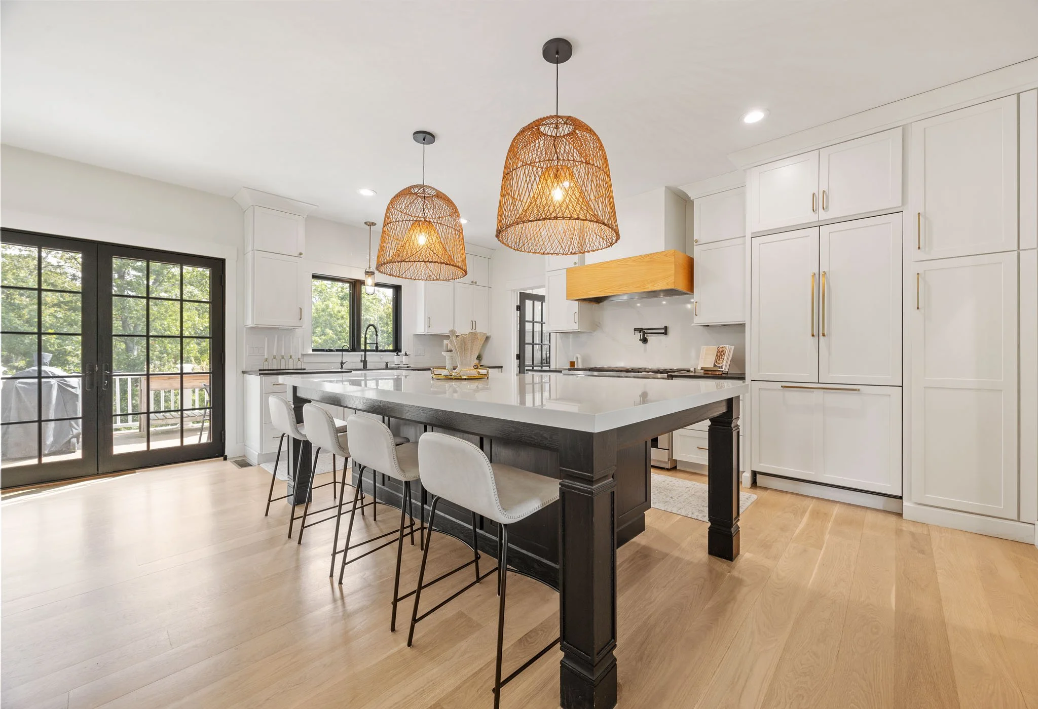 Bright, modern kitchen with white cabinets, large windows, wooden accents, and an island with stools.