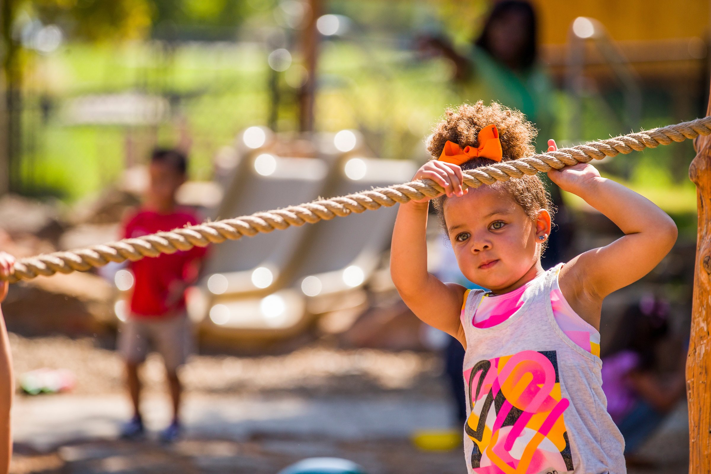 young girl hanging on to a rope for balance in an outdoor classroom as she's walking on a balance beam