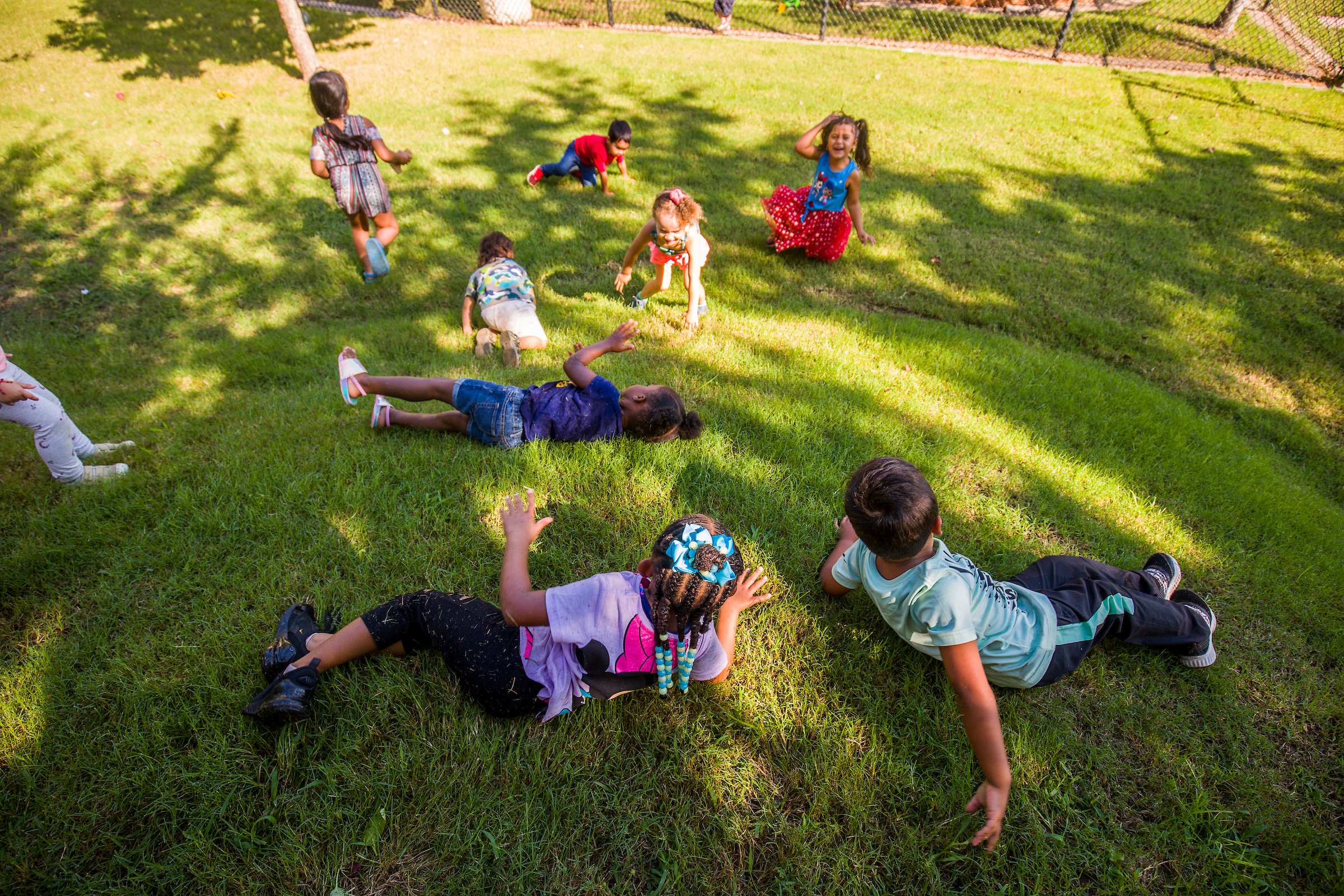 eight pre-k children rolling in the grass of a tumble hill in an outdoor classroom
