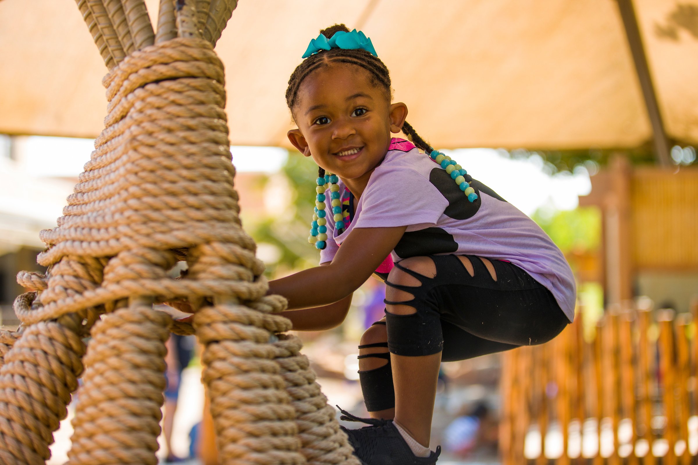 young smiling girl climbing on a rope feature in an outdoor classroom