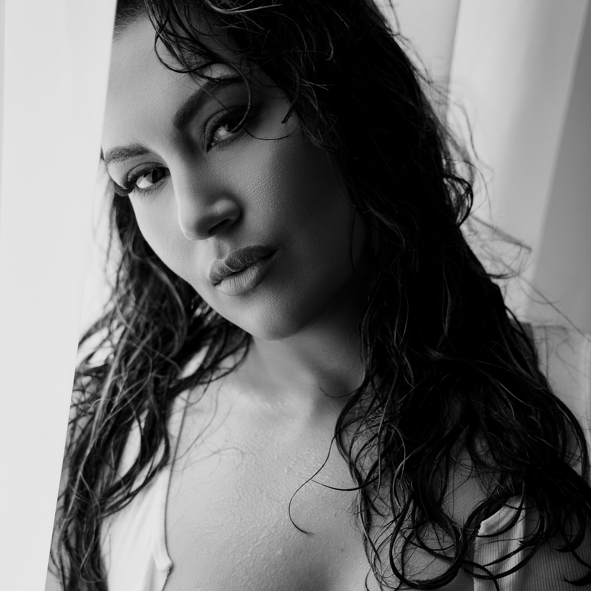 Close-up black and white photo of a woman's face, with wet curly hair partially covering her face, looking over her shoulder.