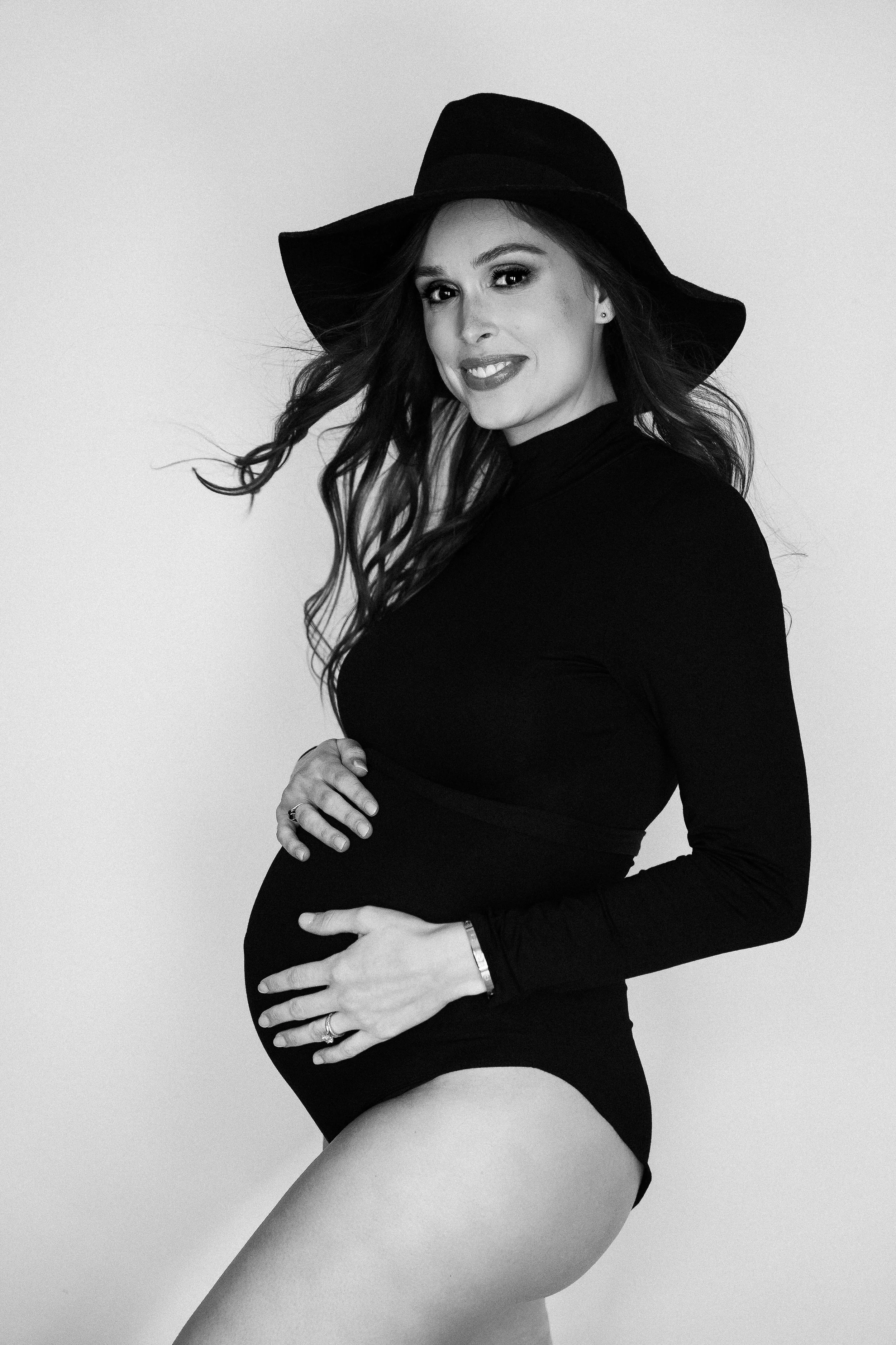 Black and white portrait of a young woman with long dark hair smiling, eyes closed, hand on her head, wearing a cozy sweater during a boudoir session at Chrissy René Studios in Round Rock, Texas