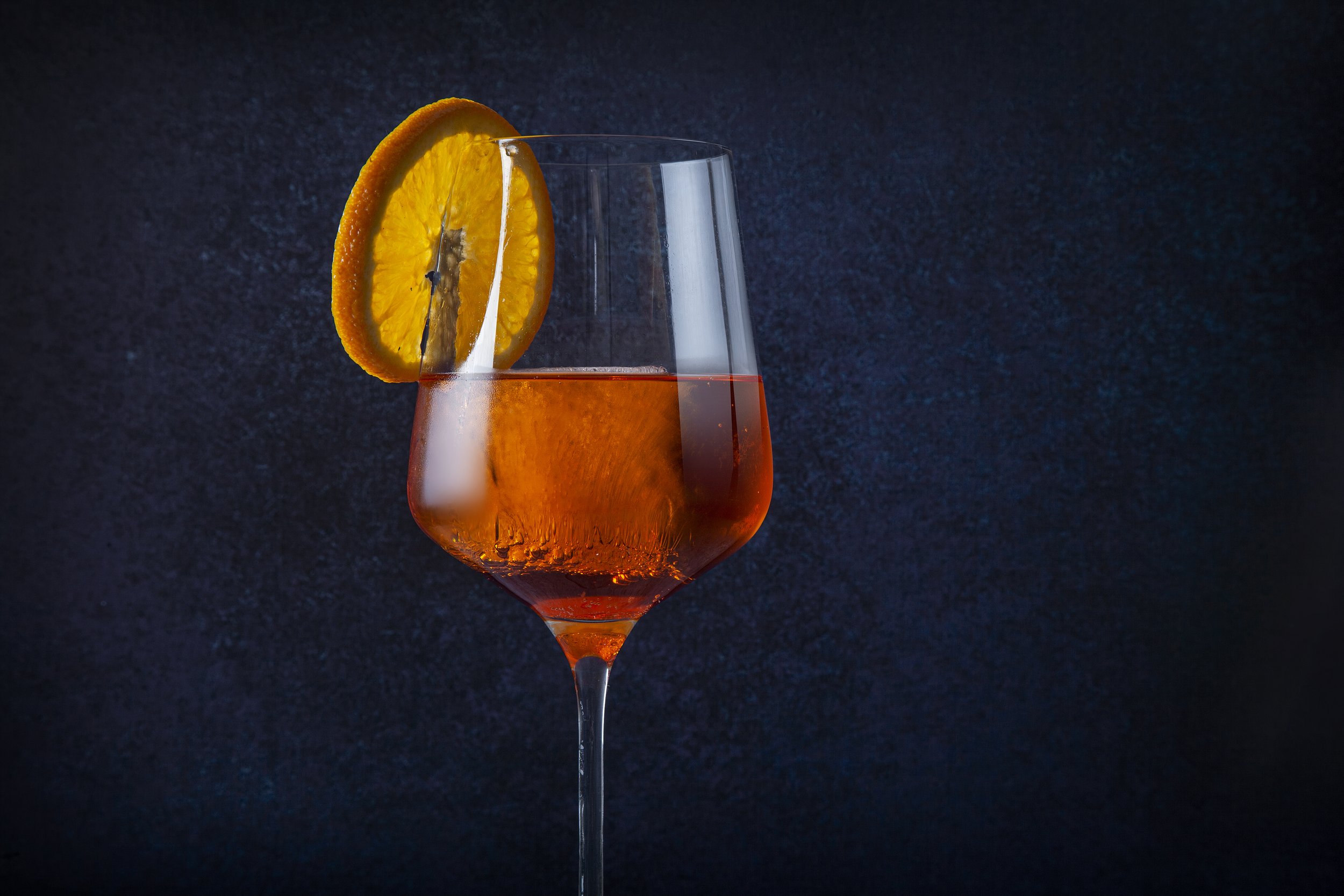 Wine glass with orange cocktail and orange slice garnish on dark background