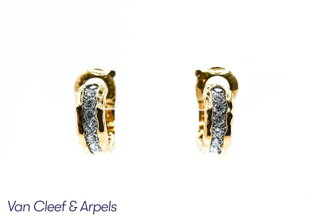 Close-up of gold hoop earrings with embedded diamonds, positioned against a white background with a partial logo and text for Van Cleef & Arpels.