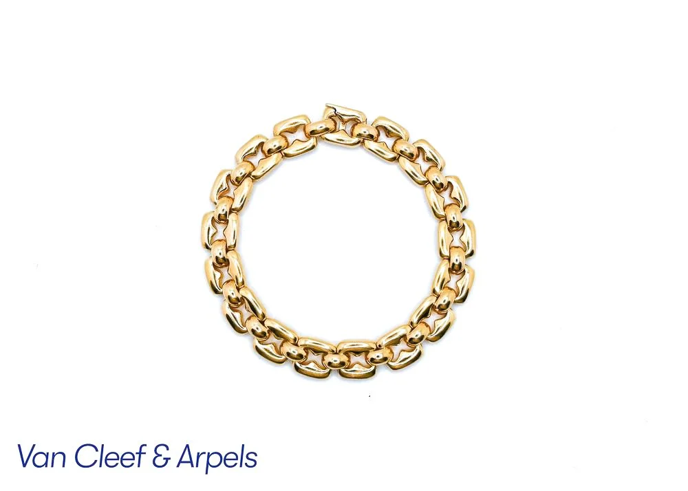 A gold chain necklace with large links, placed against a white background, with partially visible text 'Van Cleef & Arpels' at the bottom.