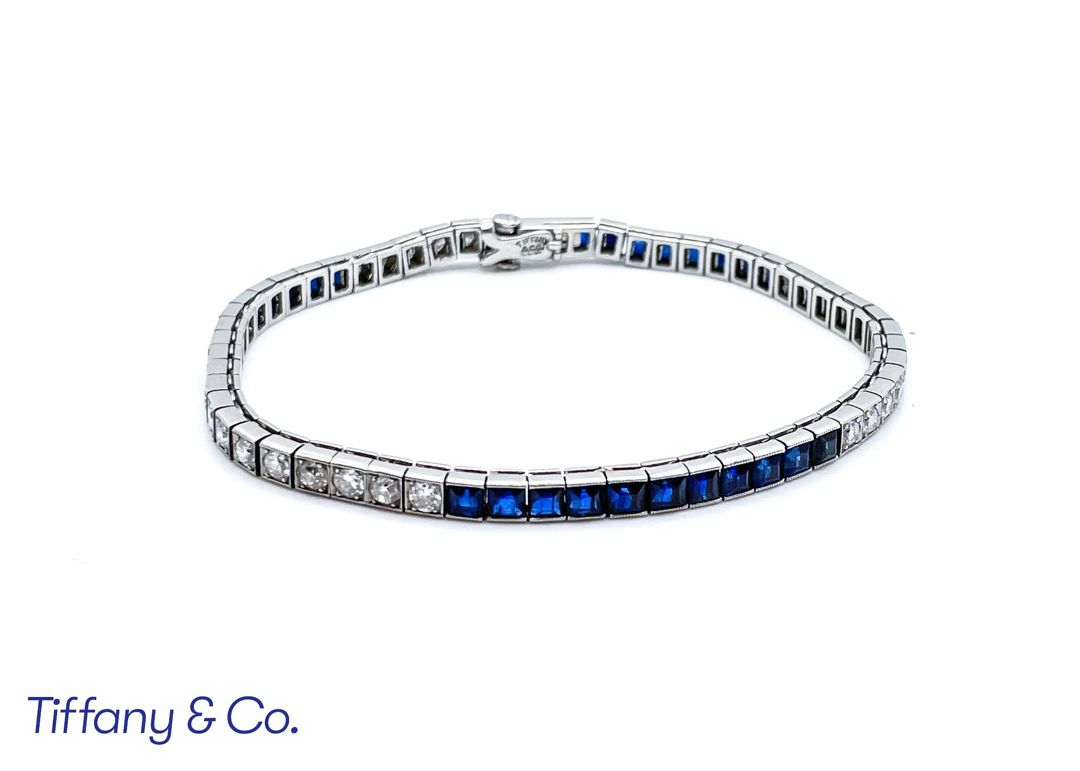 A diamond bracelet with alternating clear and blue stones, displayed on a white background, with part of the Tiffany & Co. logo visible at the bottom.