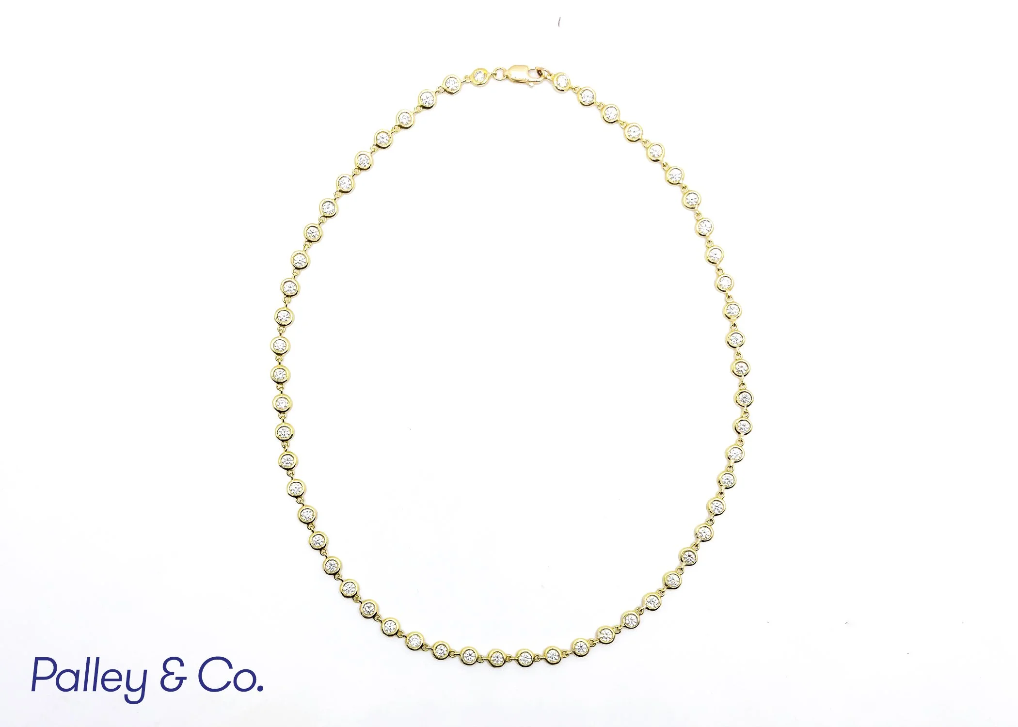 Gold necklace with round clear gemstones arranged in a line on a white background.