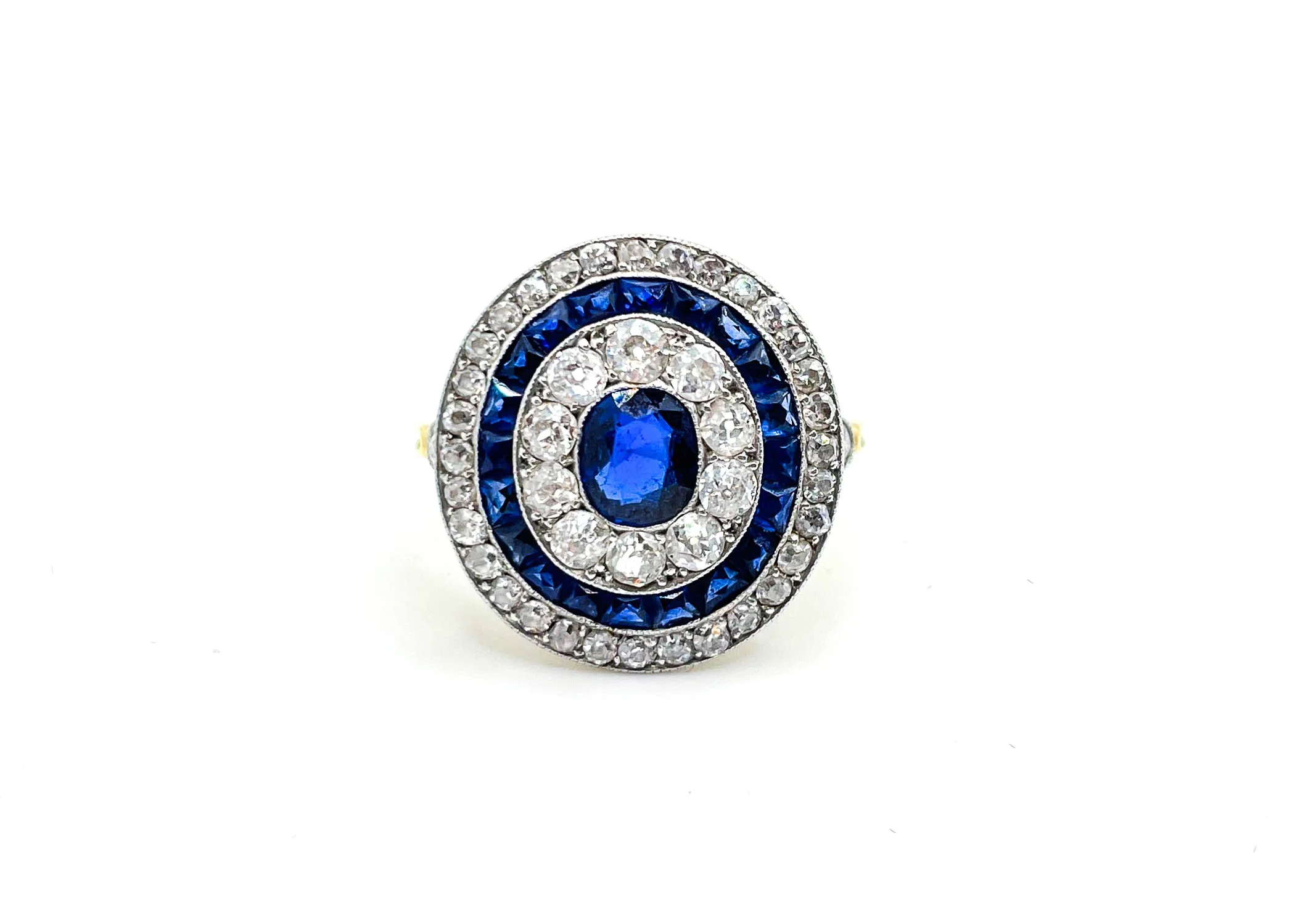 A ring featuring blue and clear gemstones arranged in concentric circles on a plain white background.