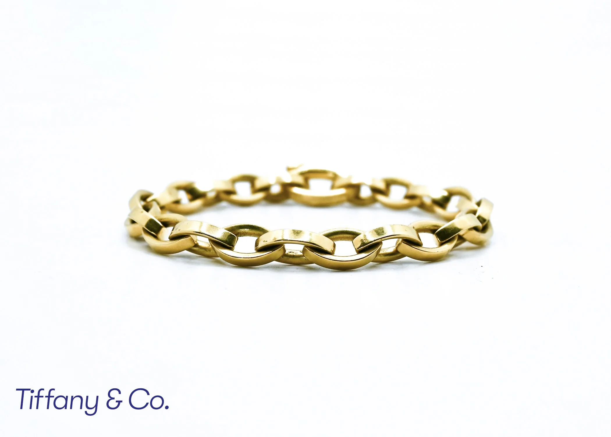 Golden chain bracelet on white background, Tiffany & Co. logo partially visible underneath.