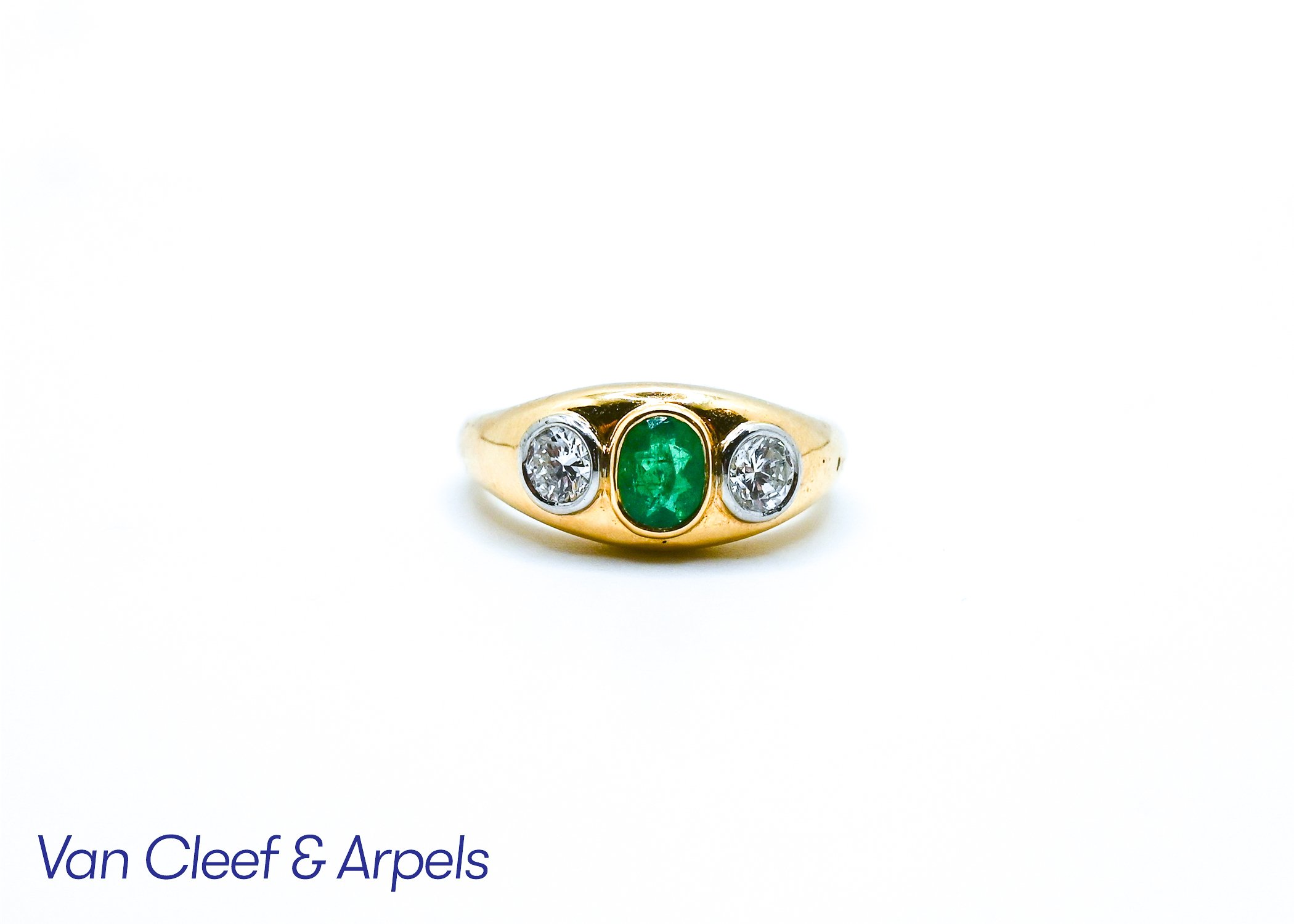 Gold ring with three gemstones, a central emerald and two diamonds set on either side.