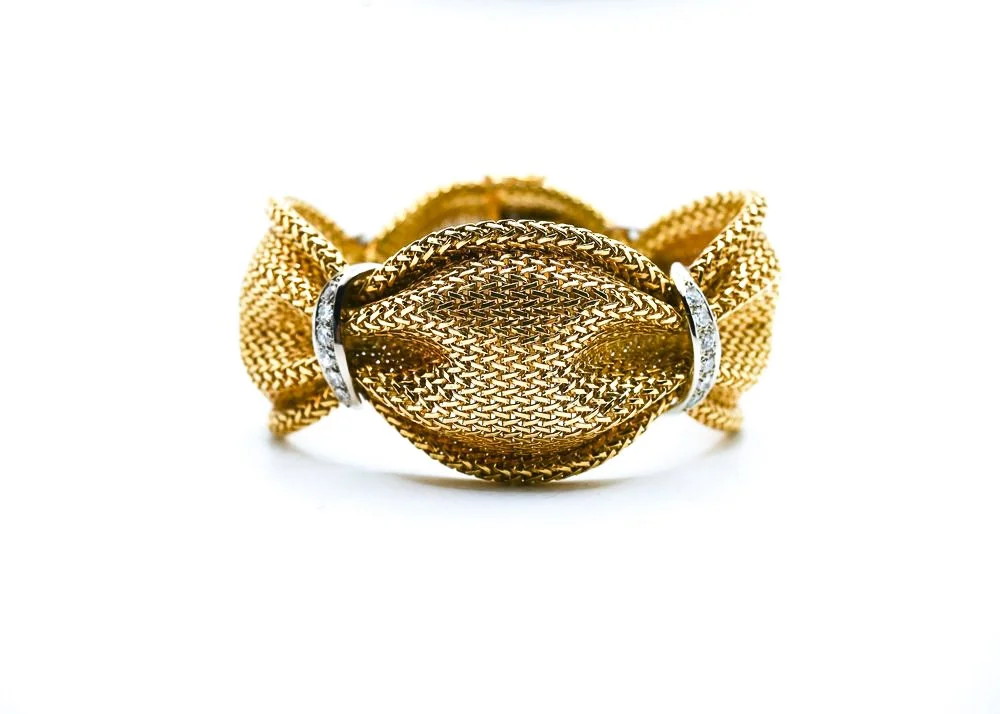 Gold-colored mesh jewelry piece wrapped with clear rings, set against a white background.