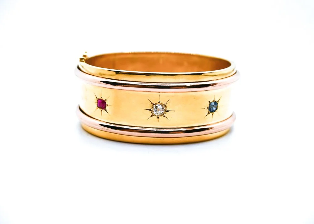 Close-up of three stacked gold rings, each adorned with small colored gemstones, against a white background.