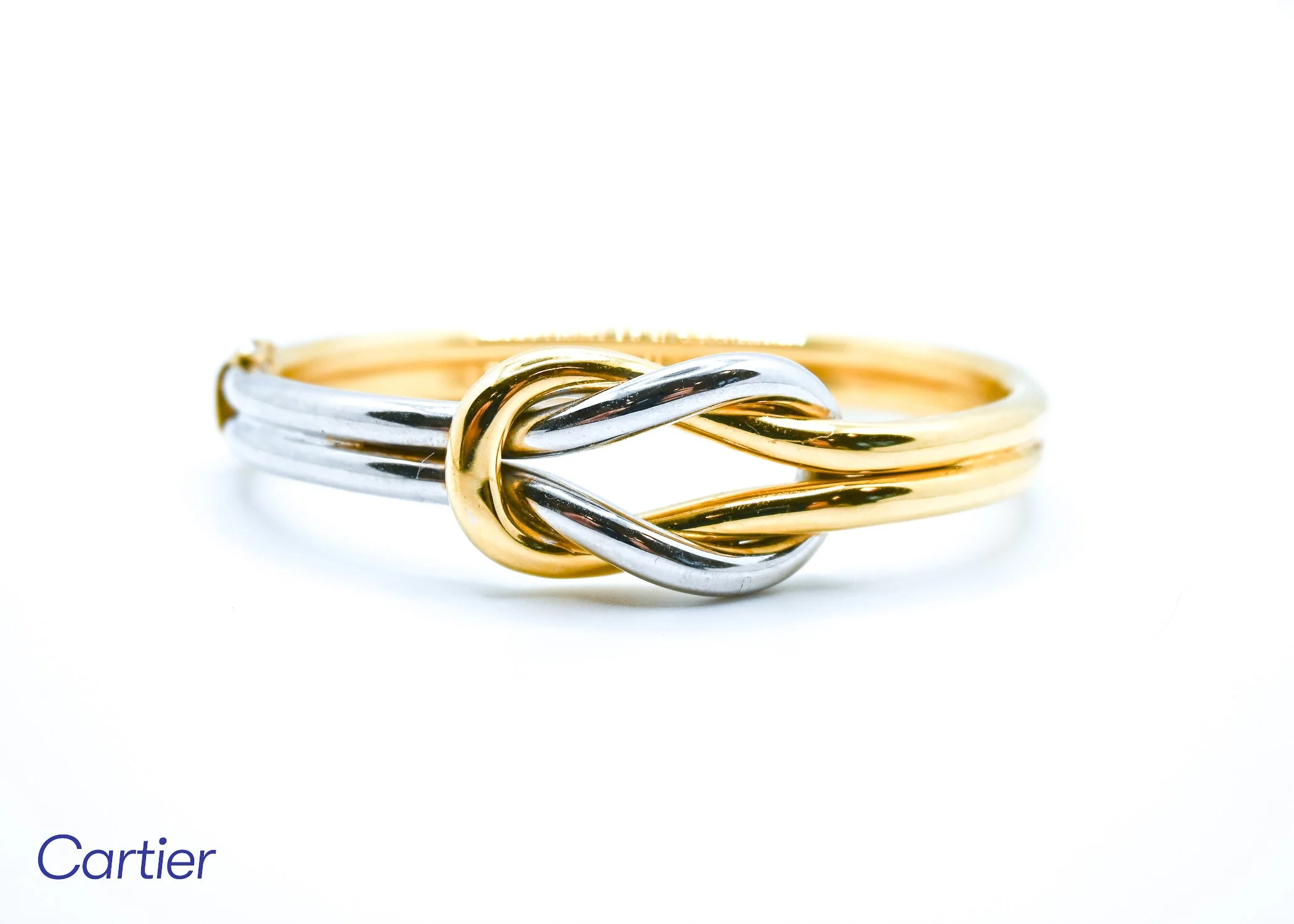 Close-up of a tricolor twisted ring with gold, silver, and rose gold bands against a white background, featuring the Cartier logo partially visible in the lower left corner.