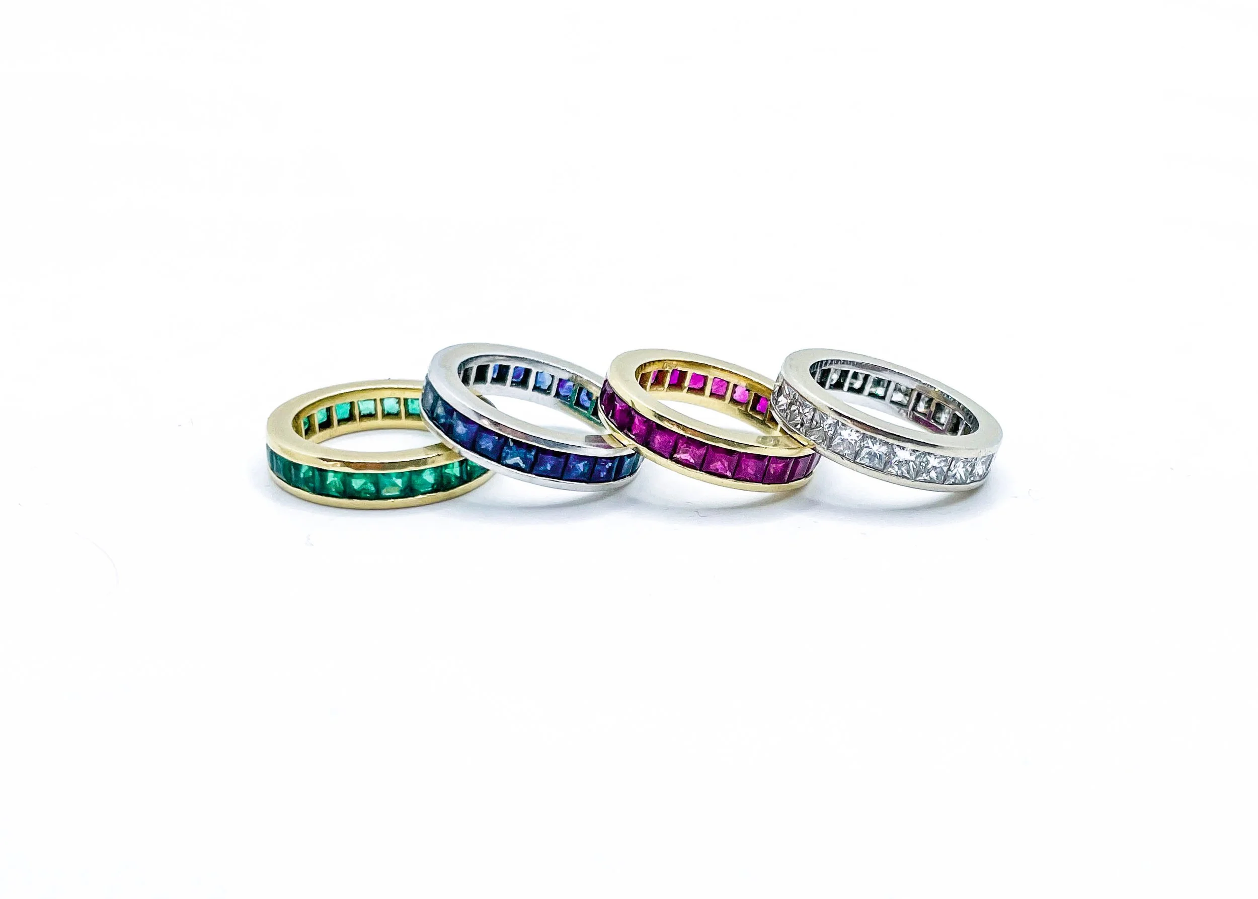 Four rings with colorful gemstones arranged in a row on a white background.