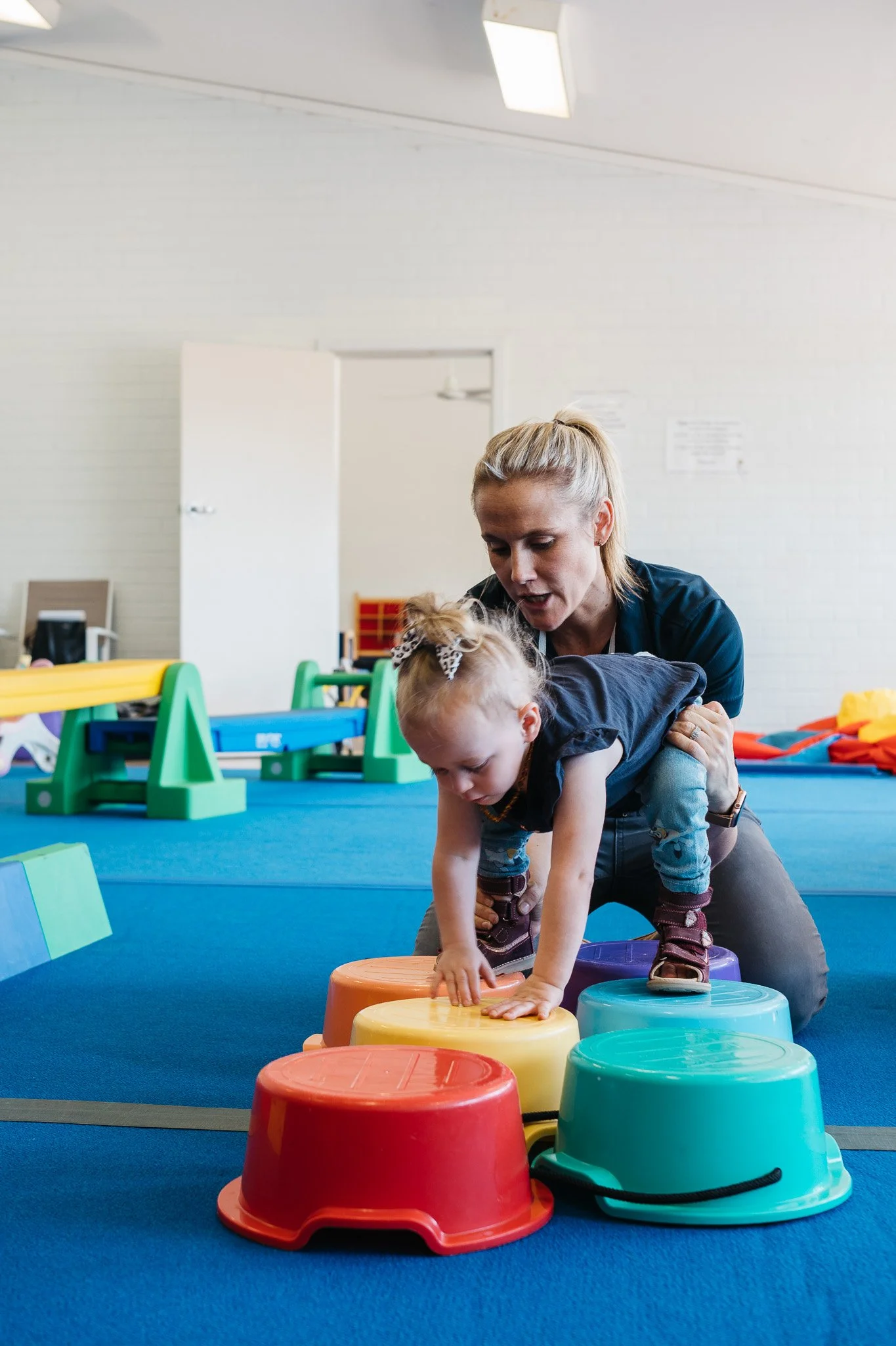 Physiotherapist helping a toddler climb colourful stepping stools in the Outreach clinic gym