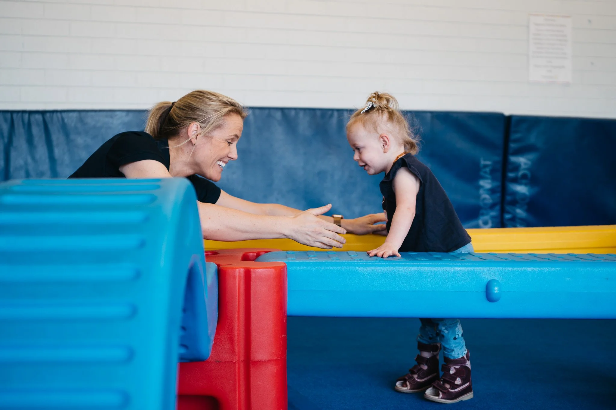 Outreach paediatric physiotherapist playing with a toddler on soft play equipment during a therapy session