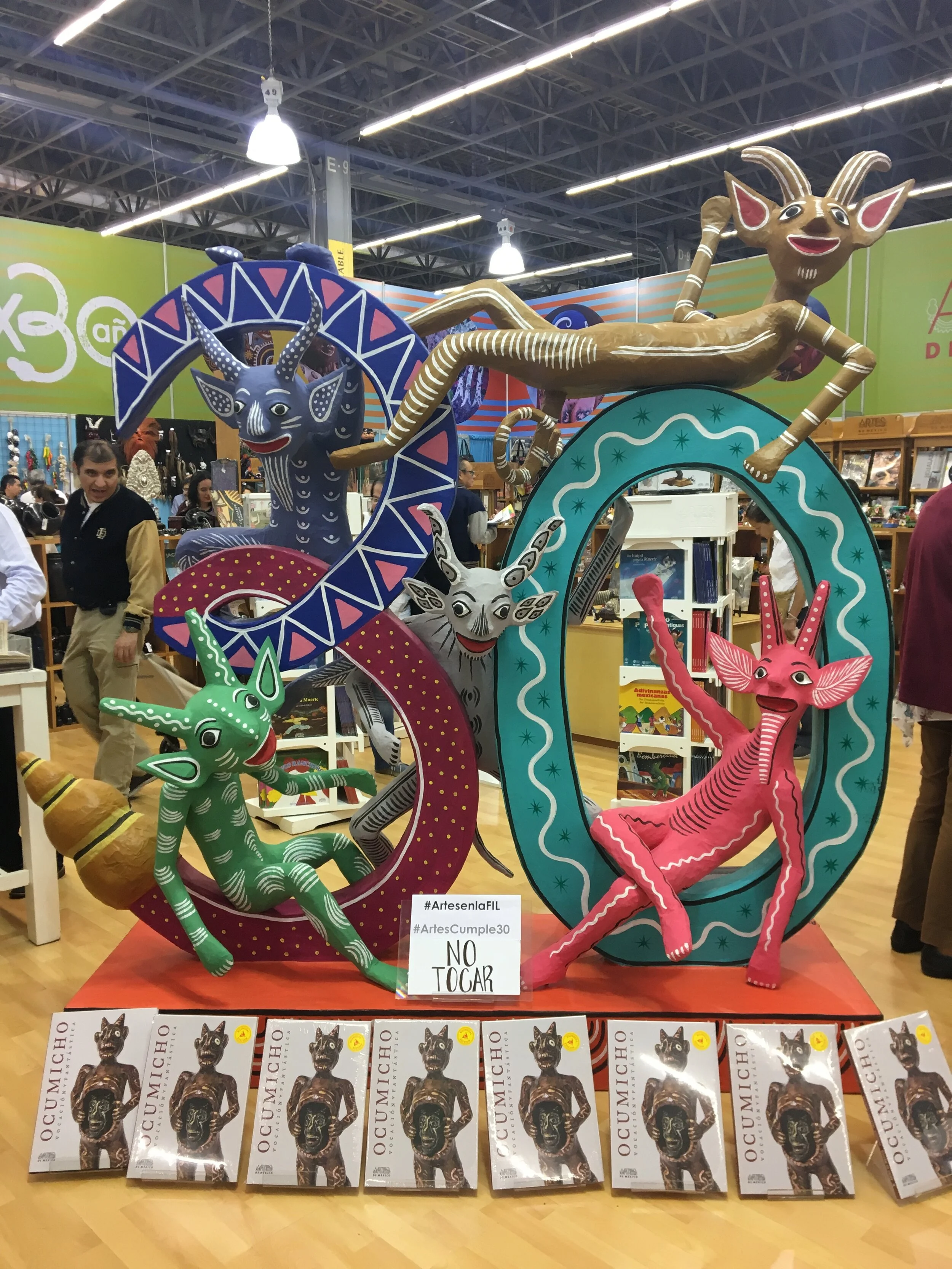Colorful art installation featuring a variety of whimsical, cartoonish animals, including a pink elephant, a green deer, and a gray goat, all positioned around large, decorative letter shapes in an indoor market or exhibit setting.
