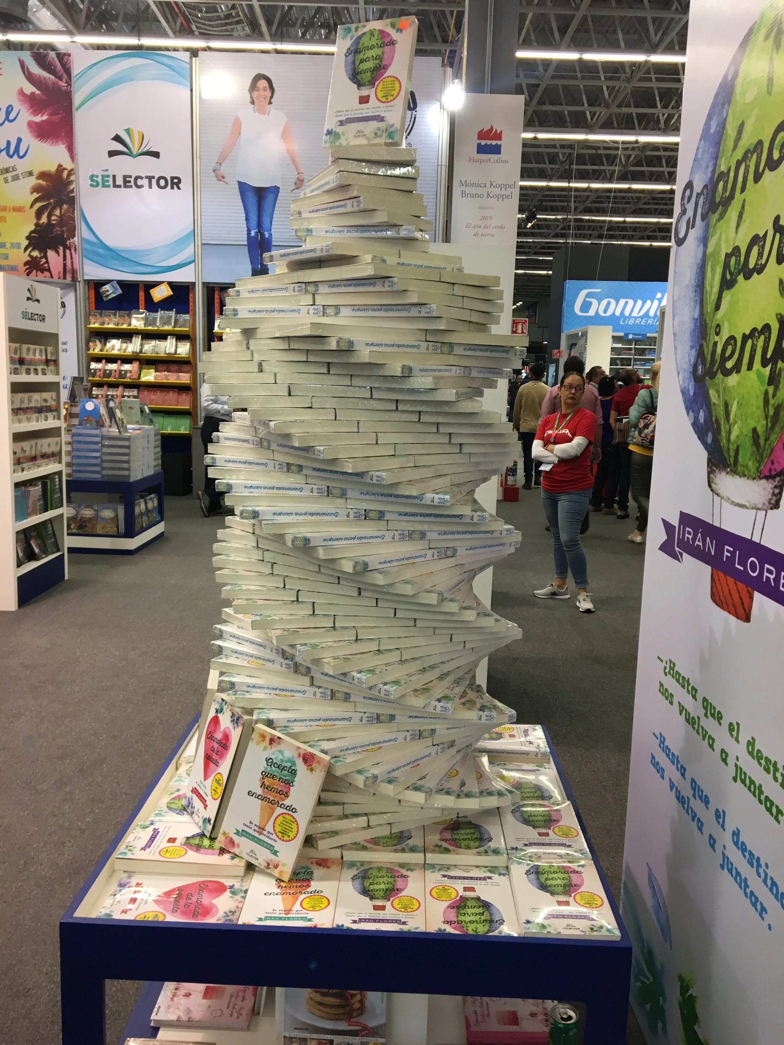 Display of math-themed books and flyers at a bookstore, with a tall, tilted stack of books in the center, and several people browsing in the background.