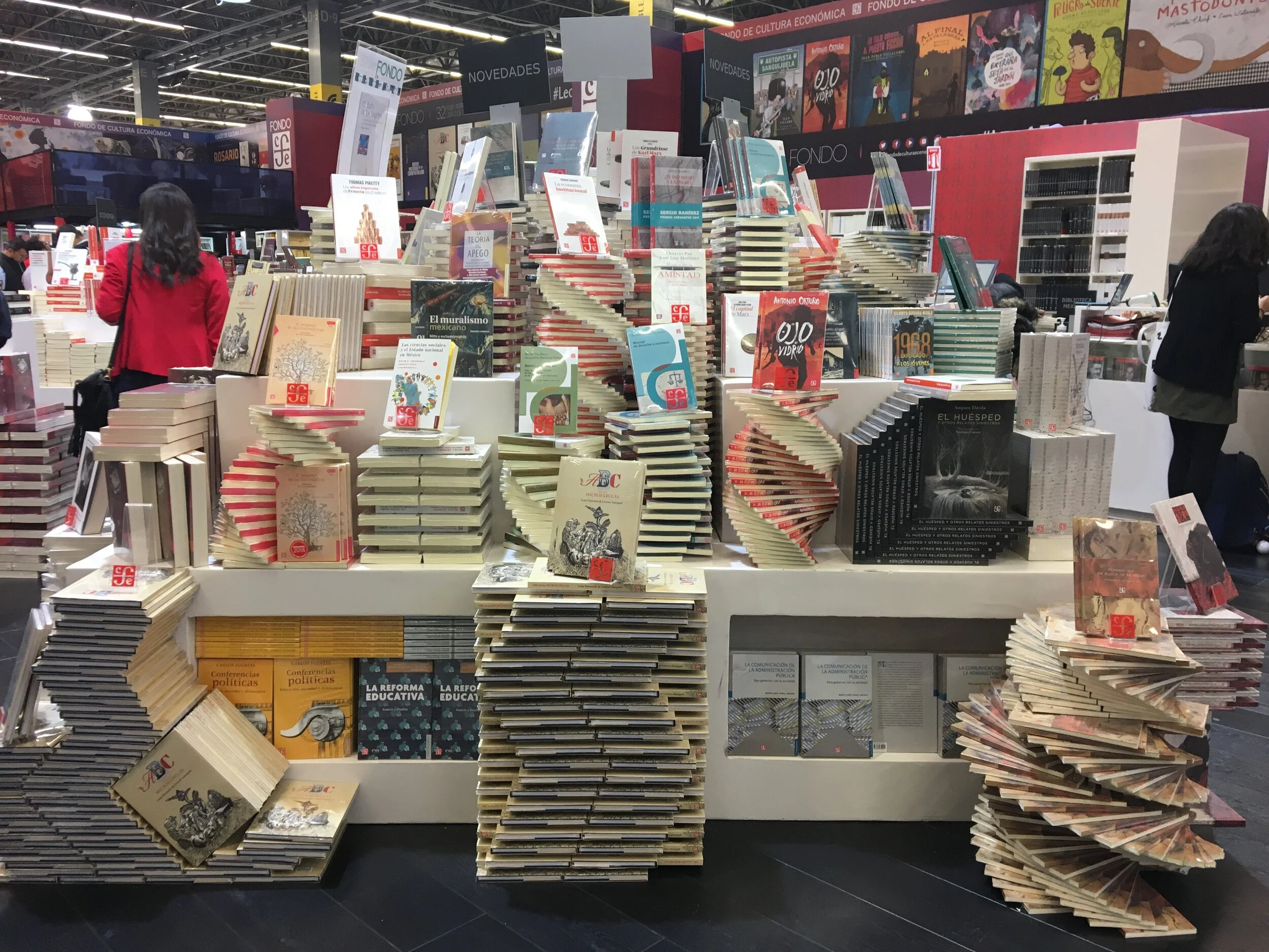 A bookstore display with stacked and arranged books, including some with accordion-style spirals, on tables and shelves. In the background, people browse and a wall features colorful book covers.