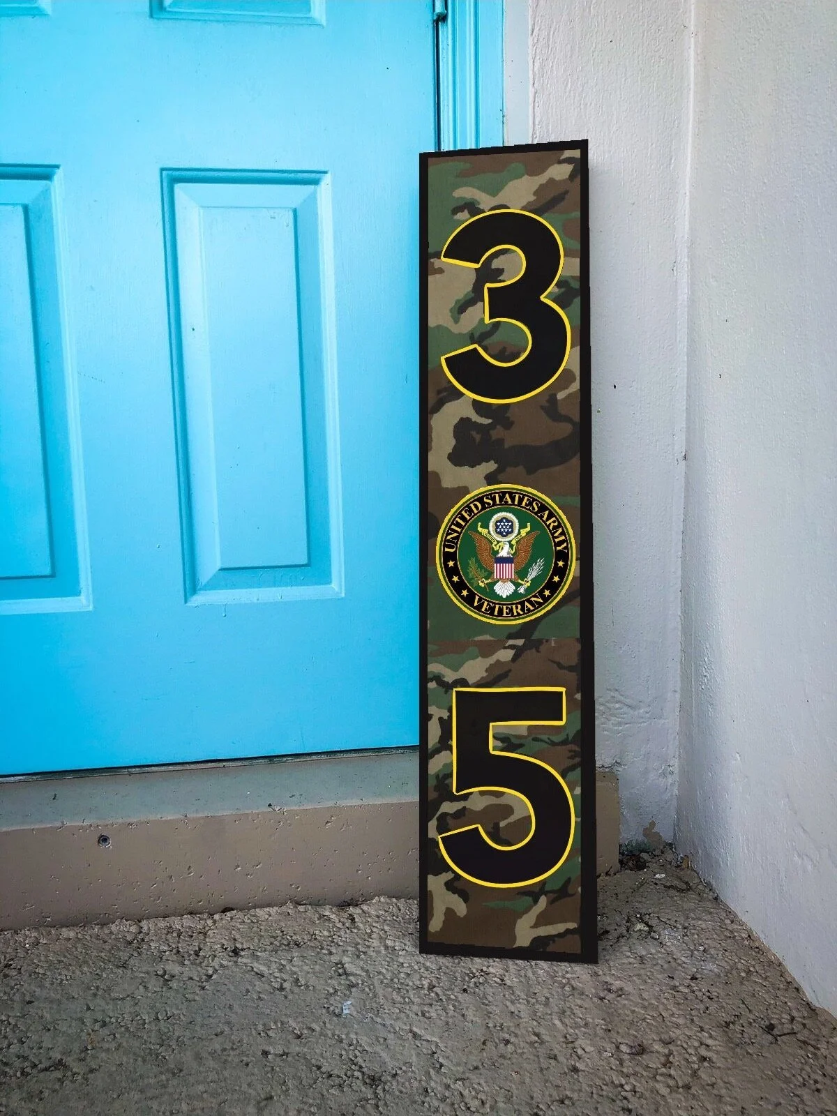 A tall sign with a camouflage background displaying the number 3 and 5 in large black and yellow font. It features the United States Army Veteran emblem and is next to a light blue door with white walls and a concrete floor.