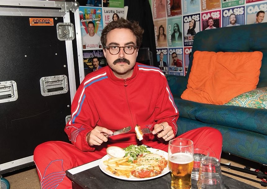 Daniel Muggleton at a table eating wearing a red track suit