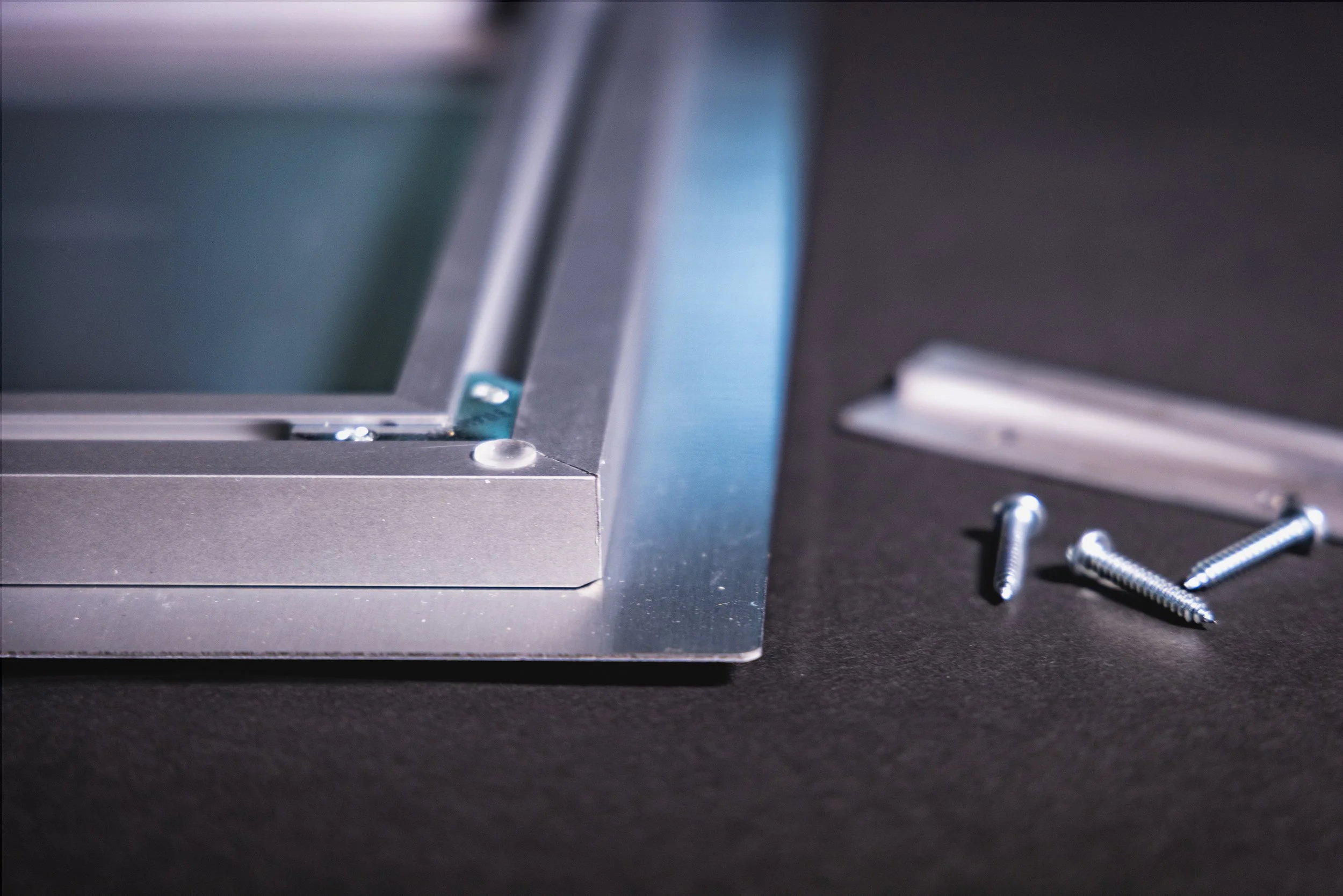 Close-up of a metallic frame with screws and a plastic part on a black surface.