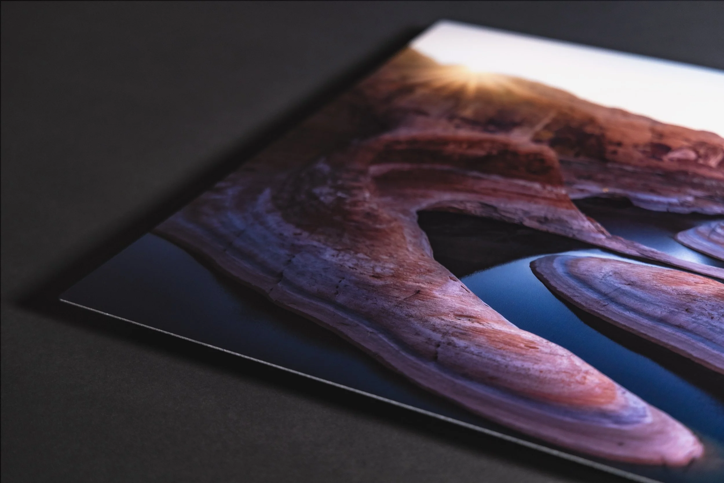 Close-up of a tablet screen displaying a landscape photograph of layered rocks and a body of water at sunset