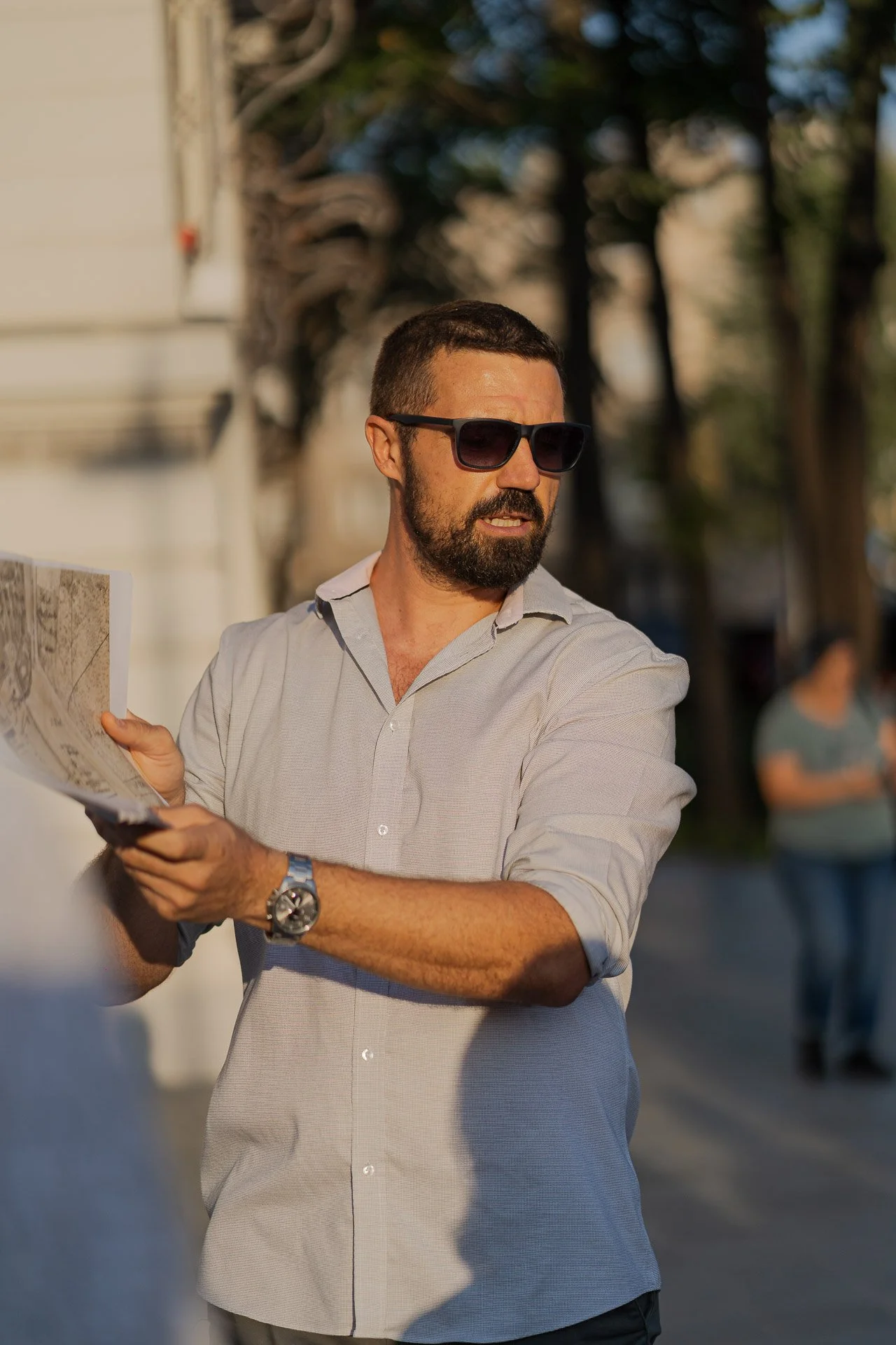 A man with a beard and sunglasses holding a map outdoors on a sunny day.