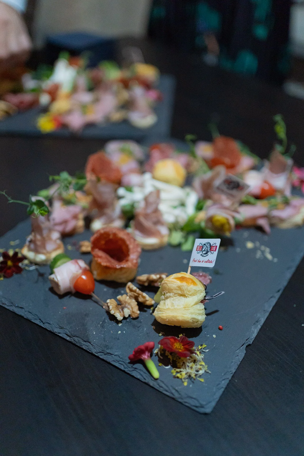 Assorted gourmet bite-sized appetizers and finger foods on a black slate serving platter, garnished with edible flowers and walnuts.