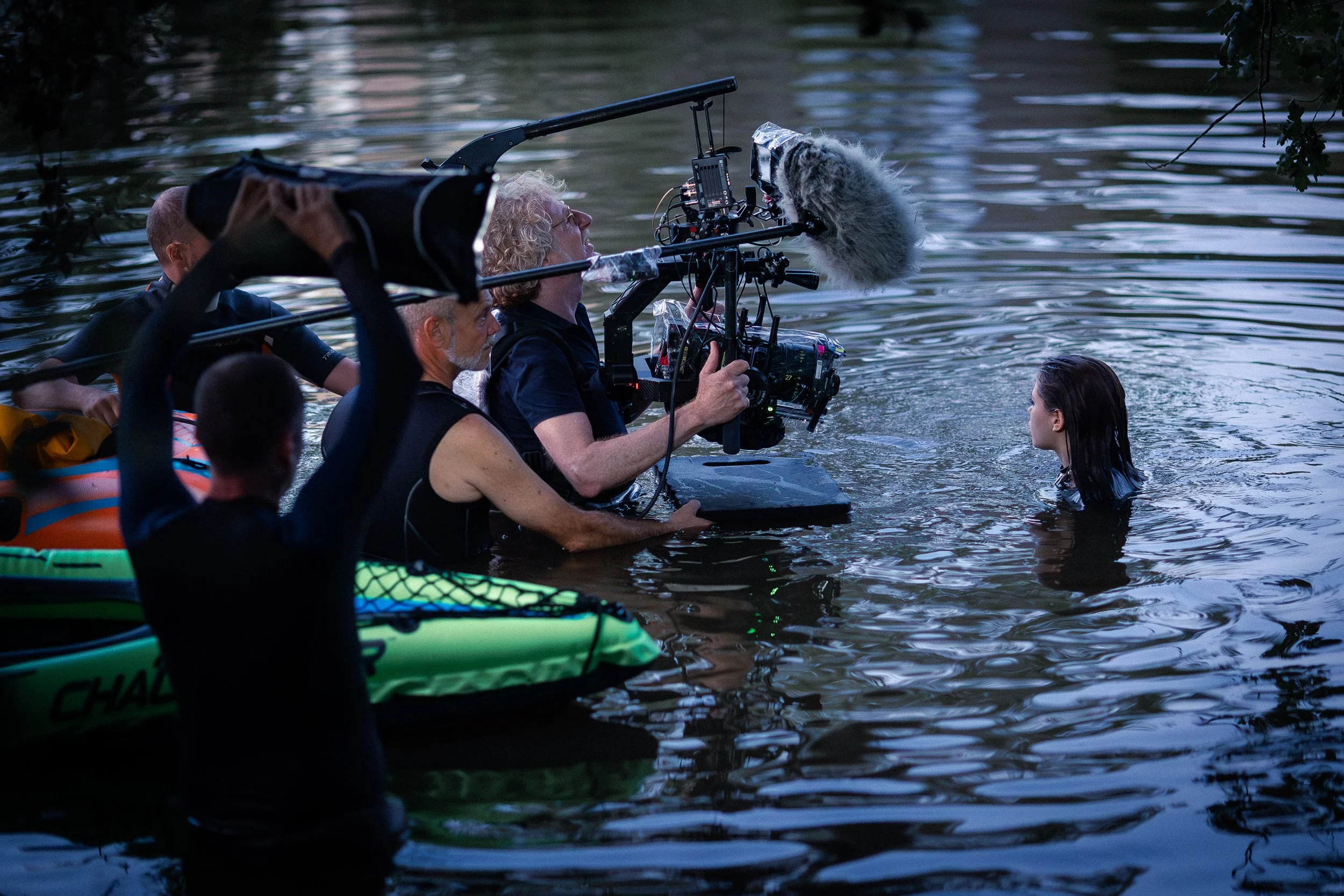 Une équipe de tournage en kayak dans une rivière, utilisant du matériel audiovisuel pour filmer une femme dans l’eau.