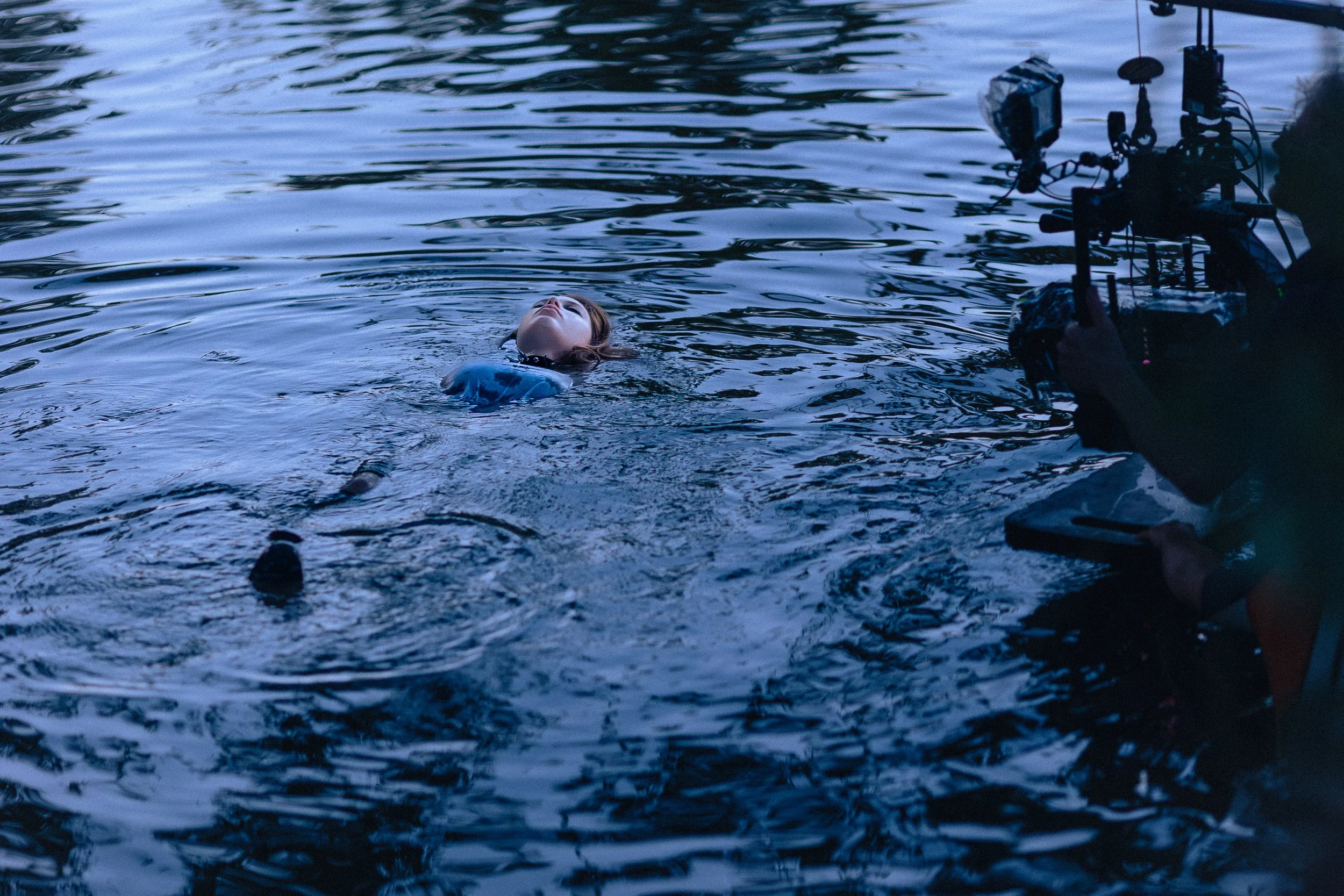 Une personne nage dans un corps d'eau sombre, avec un équipement de tournage ou de photographie à proximité.
