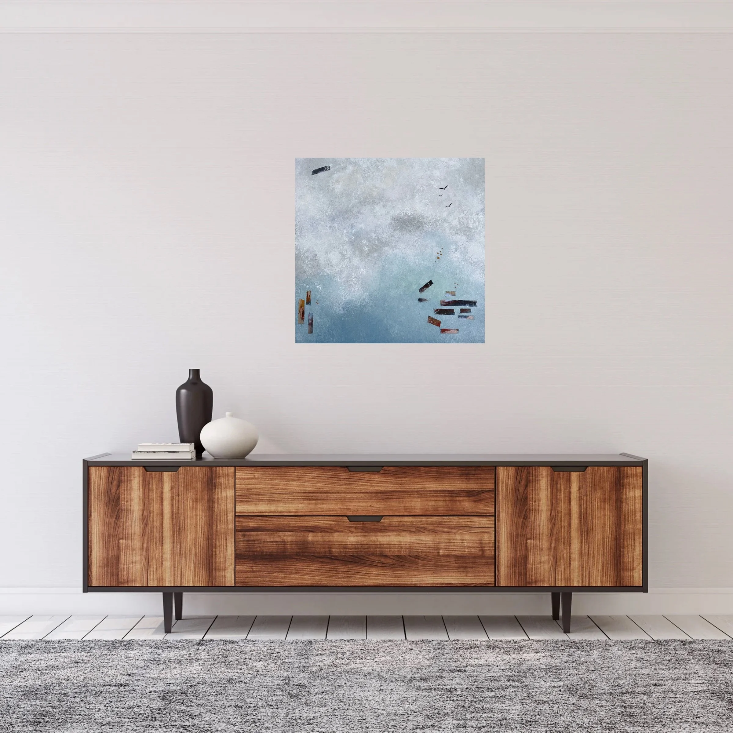A mid-century modern wooden sideboard with black accents against a white wall, decorated with vases and books, and a painting of a cloudy sky with boats hanging above.