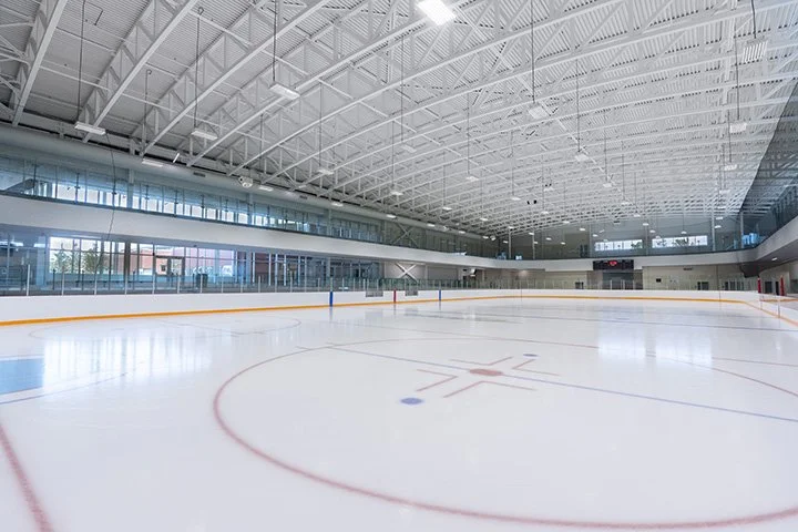 Empty indoor ice hockey rink with glass barriers and high ceiling in a modern sports arena.