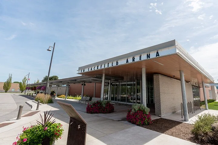 Exterior of a sports arena with a modern design, featuring a covered entrance, brick walls, and colorful flower beds in front.