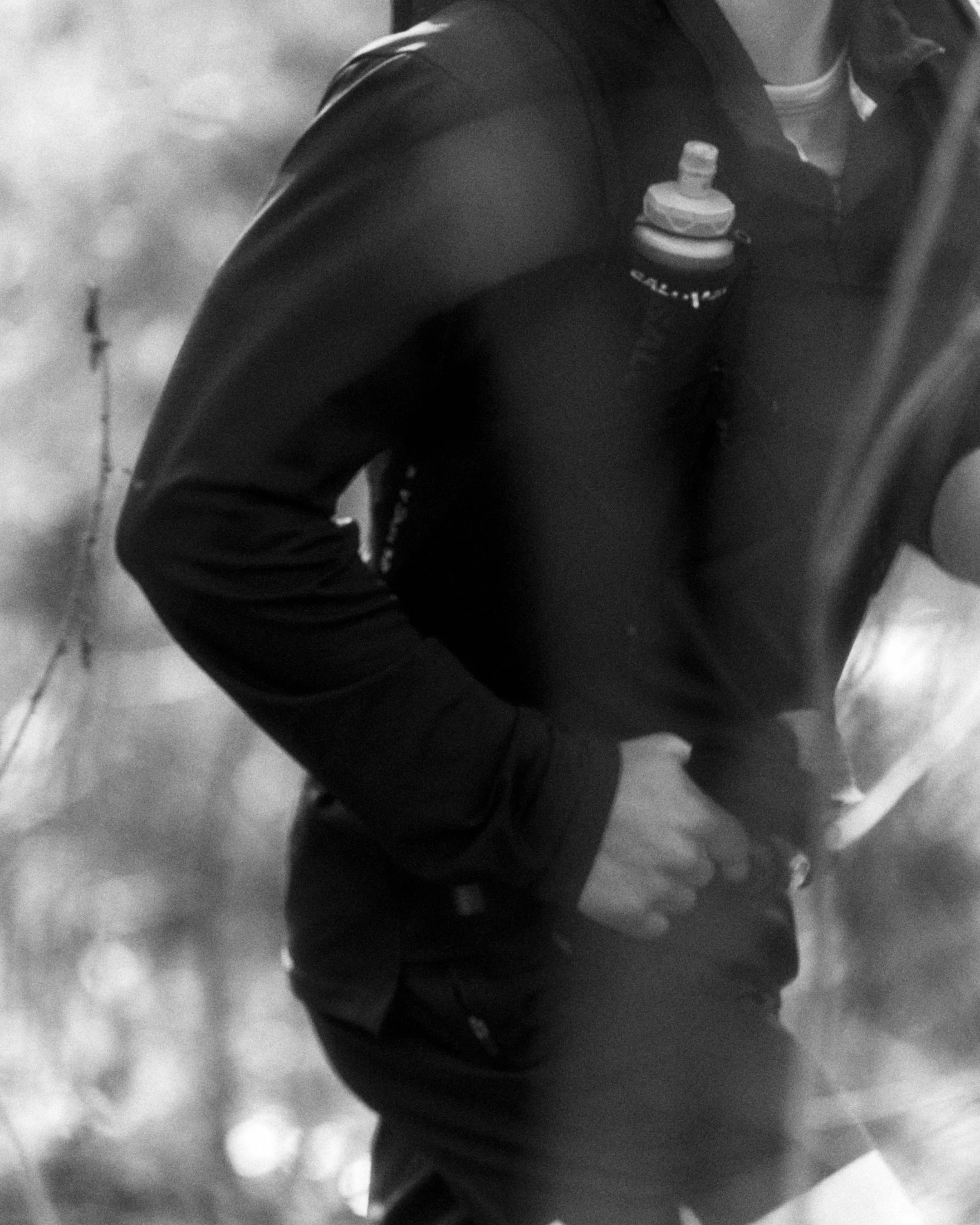 Close-up black and white photo of a person wearing a jacket with a water bottle in the side pocket.