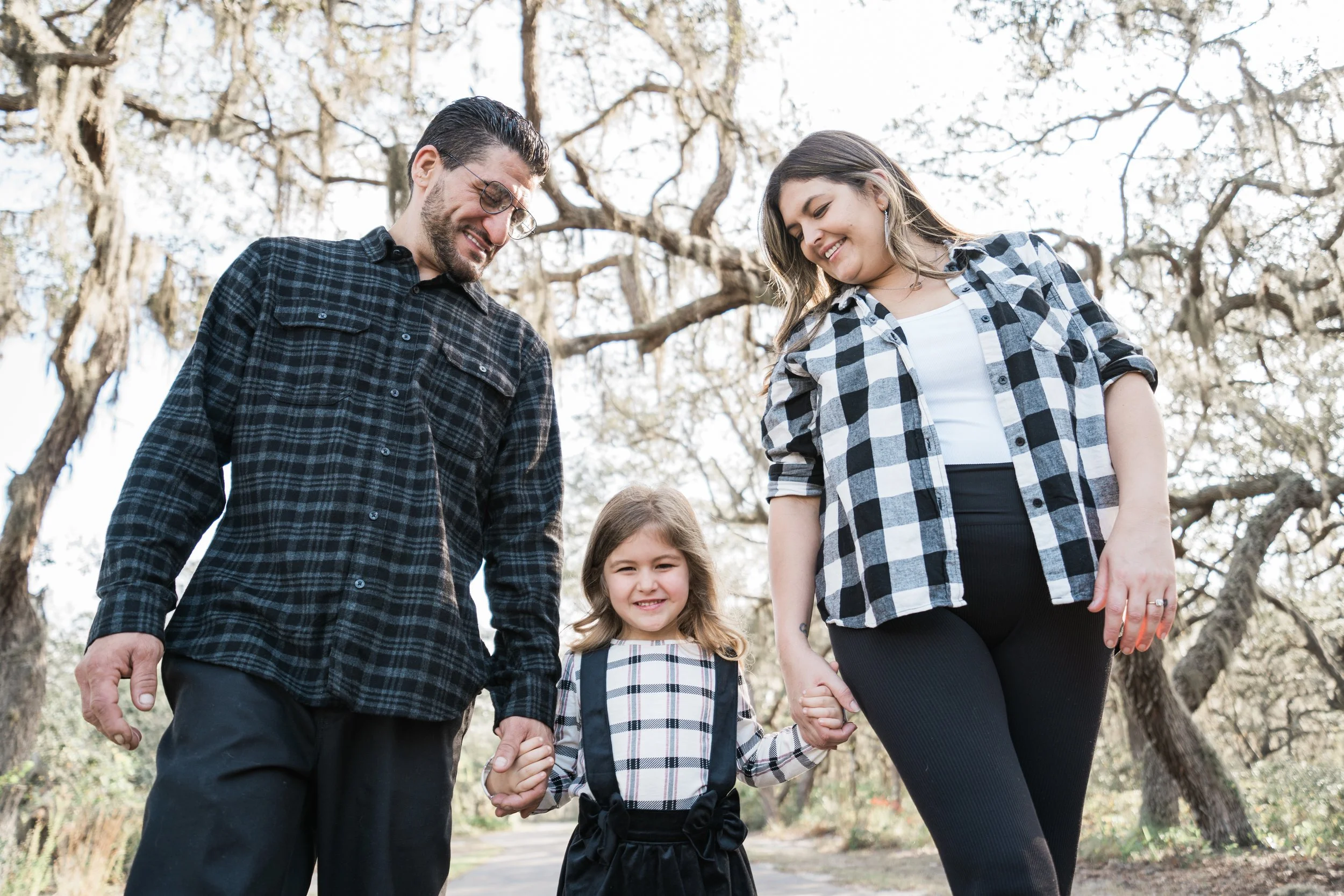 Family of three walking in a park with leafless trees, holding hands and smiling.