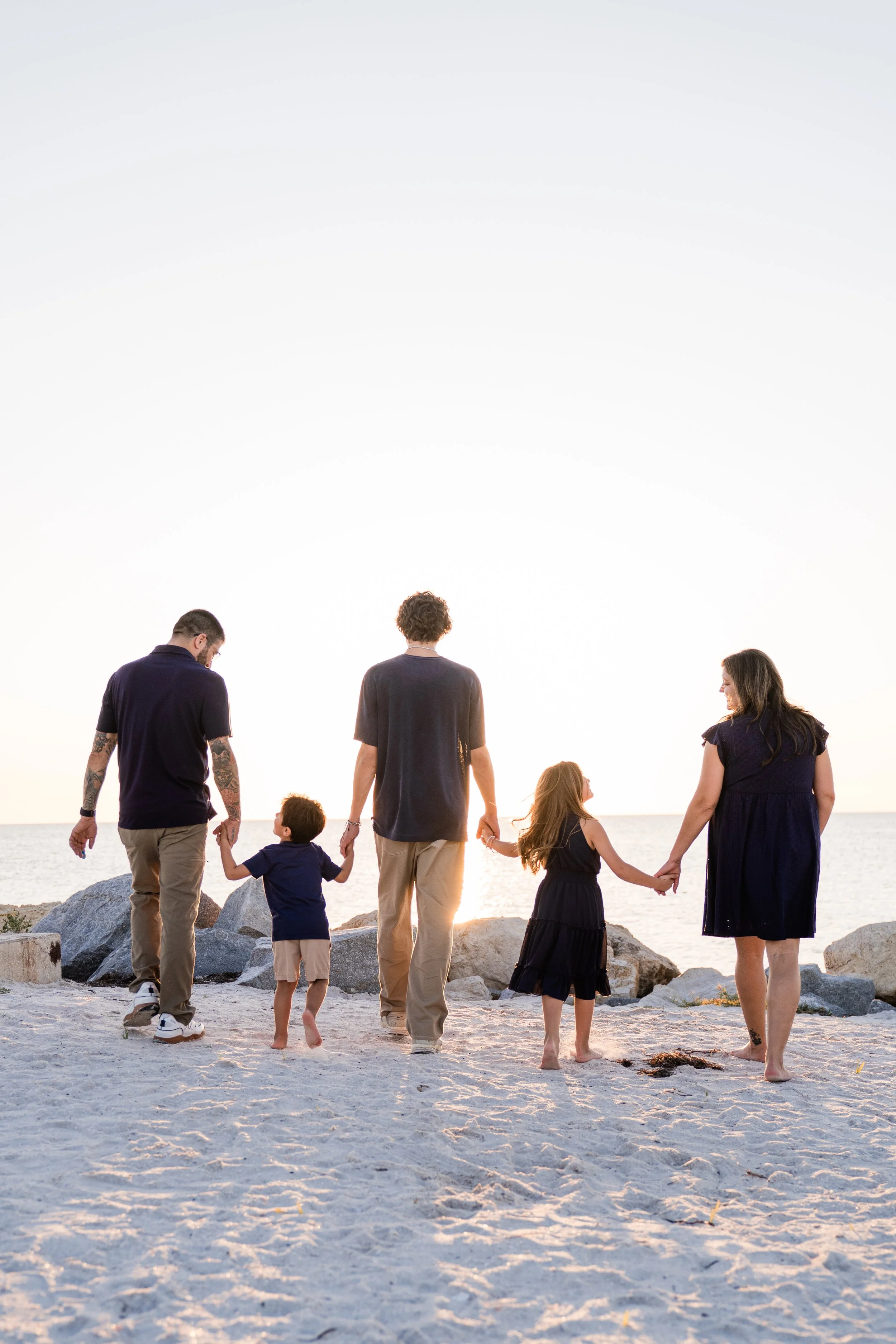 Family of five holding hands and walking on a beach during sunset.