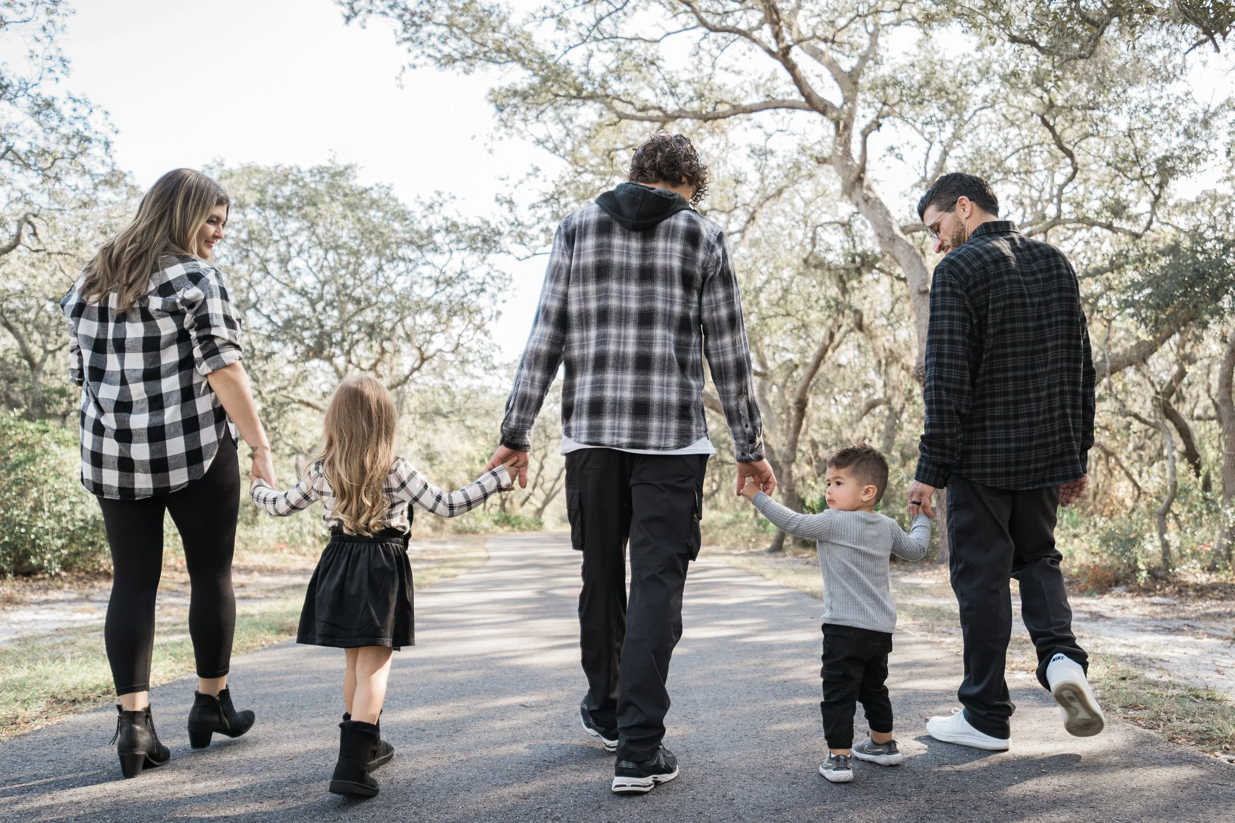 A family of six walking hand in hand on a park pathway surrounded by trees.