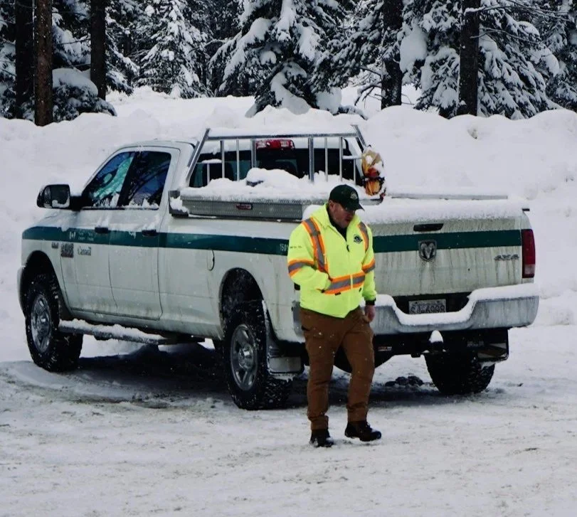 A man in a yellow jacket walking away from a truck stopped in snow