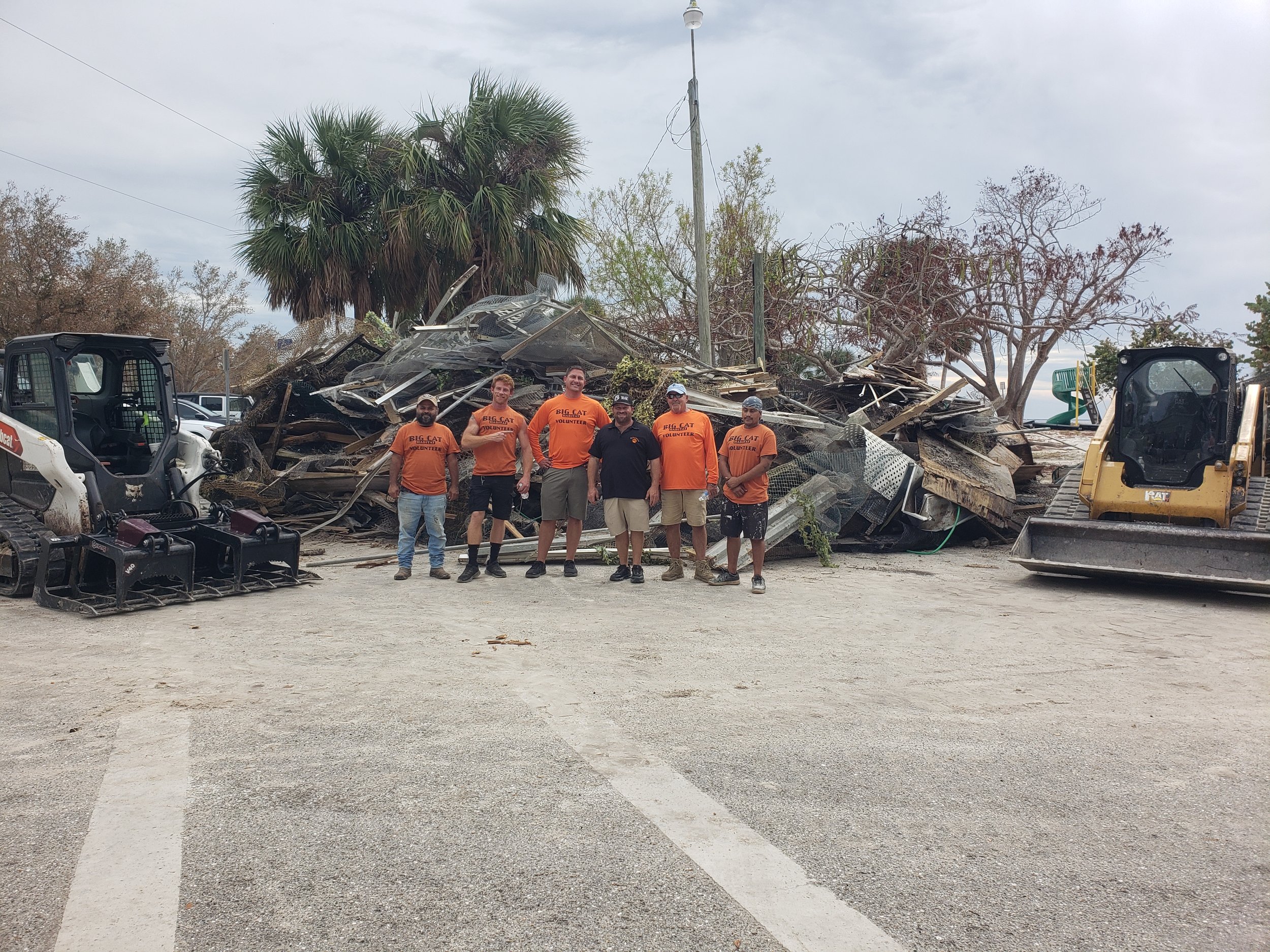 Big Cat Habitat crew poses in front of large debris pile cleared from impacted facility