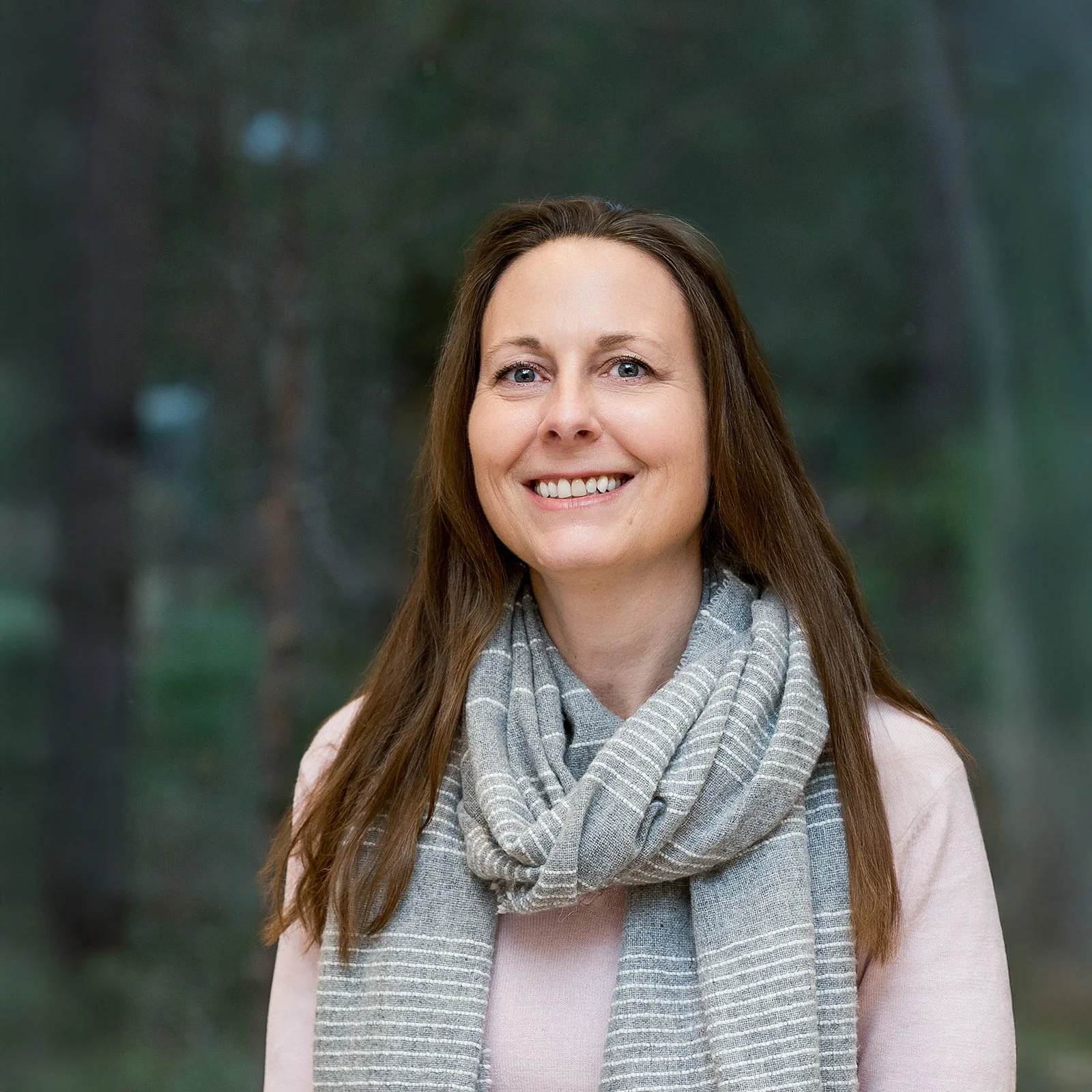 Smiling woman in a professional outdoor portrait wearing a grey scarf and pink top