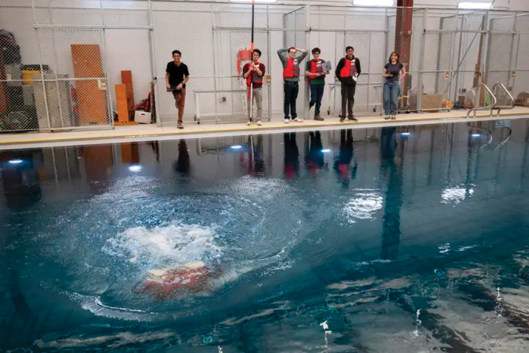 Six students stand at the edge of the RIC’s water tank operating an underwater robot.