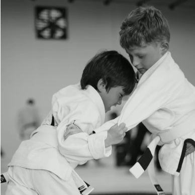 Two children in judo uniforms practicing a bow in a dojo.
