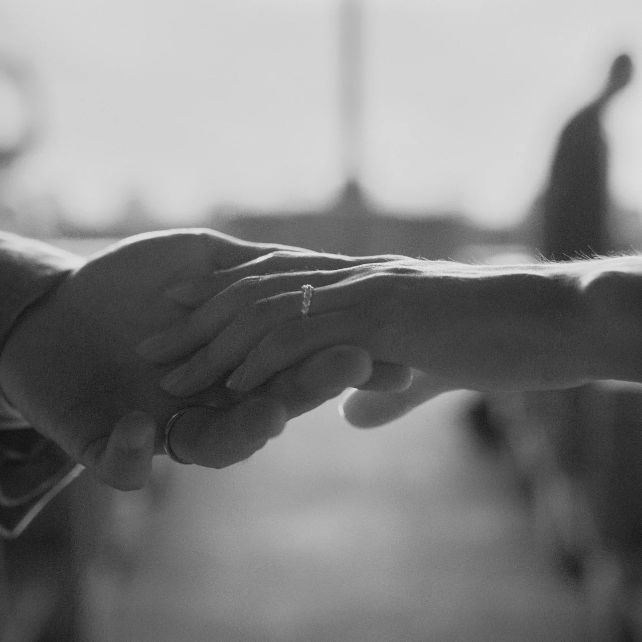 Black and white photo of two hands gently holding each other, with rings on fingers, in a close-up shot.