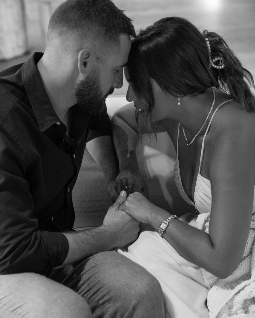 A black and white photo of a couple with foreheads touching, holding hands, and deeply engaged in an intimate moment.