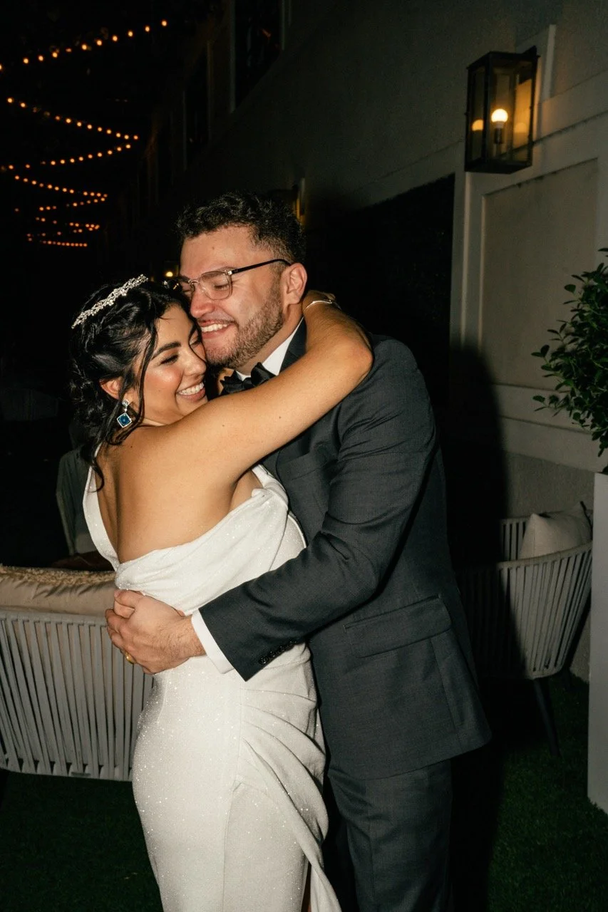 A happy couple hugging at their wedding reception, with warm outdoor lighting and a cozy atmosphere.