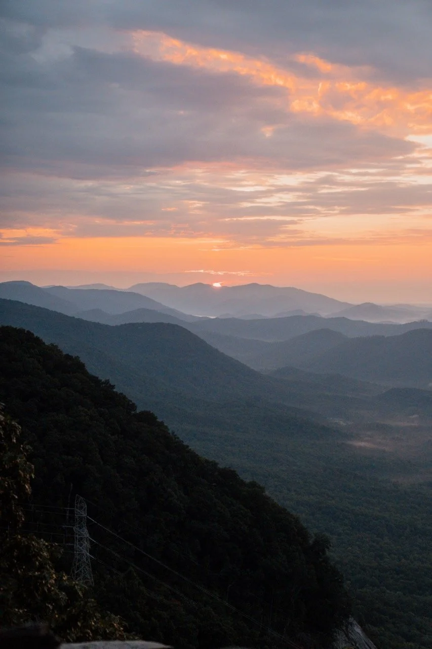 Sunset over layered mountain ranges with cloudy sky and orange and purple hues.
