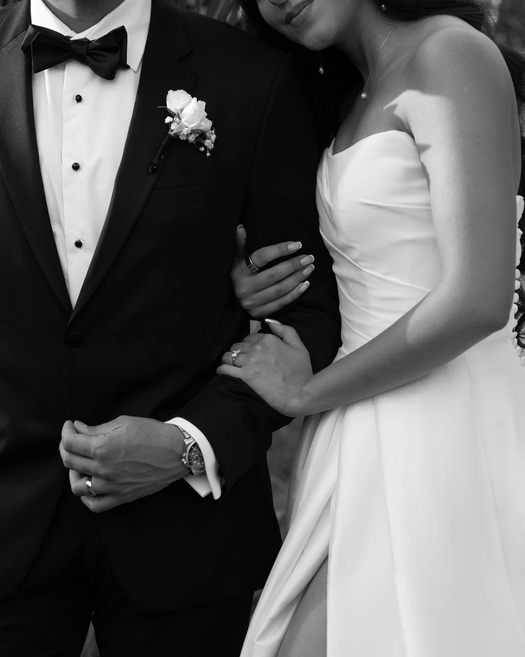 A bride and groom in wedding attire, with their arms around each other, holding hands.